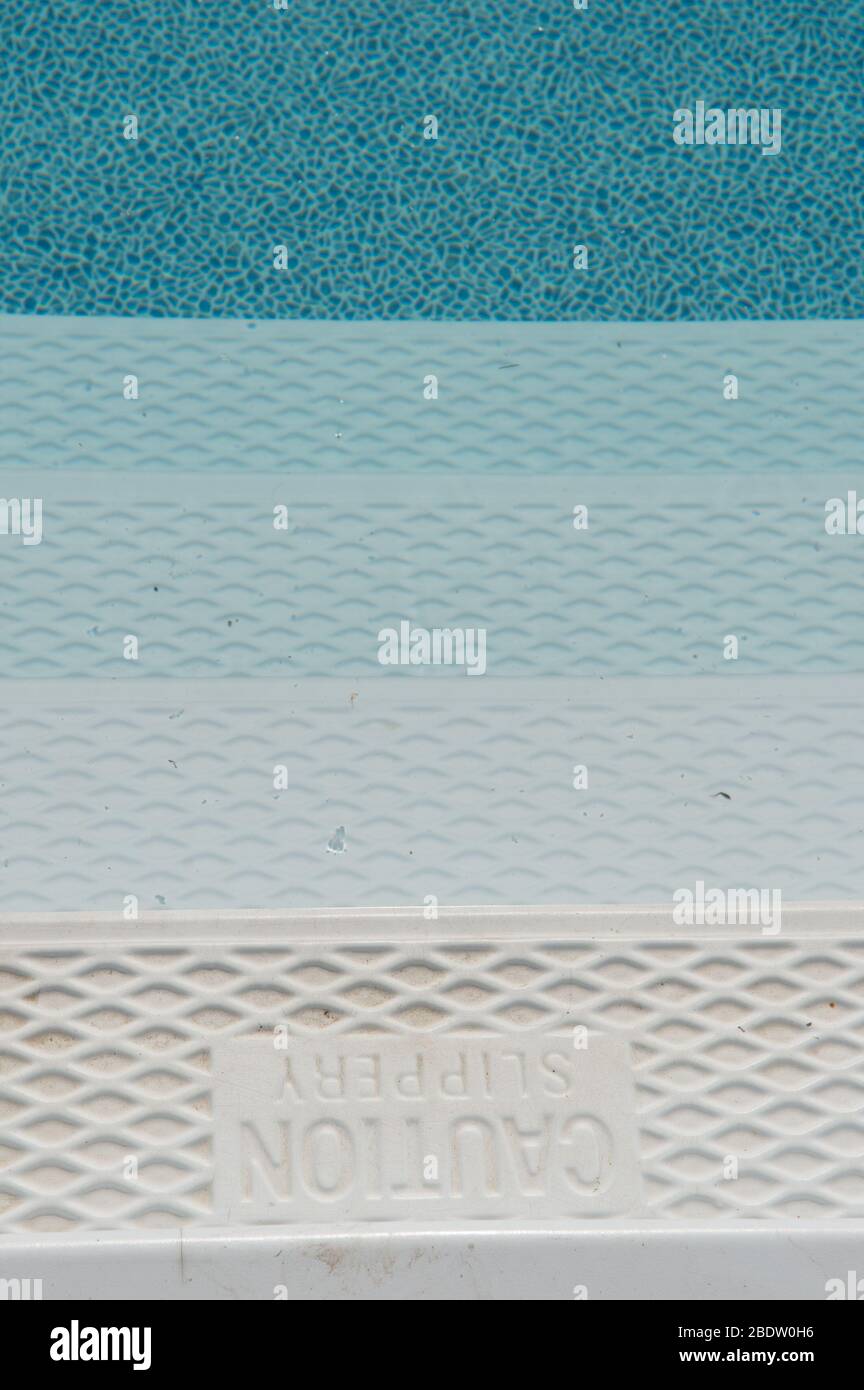 Les marches d'une piscine avec panneau glissant attention imprimé sur les marches sont couvertes d'eau avec différentes nuances de blanc puis de bleu descendant des marches Banque D'Images