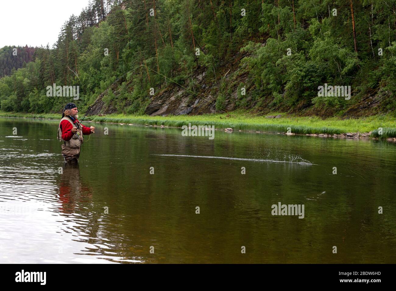 Vue latérale portrait d'un pêcheur brutal d'âge debout au niveau de la hanche dans une rivière étroite en forêt au moment de pêcher le poisson par un pêche. Passe-temps actif, h Banque D'Images