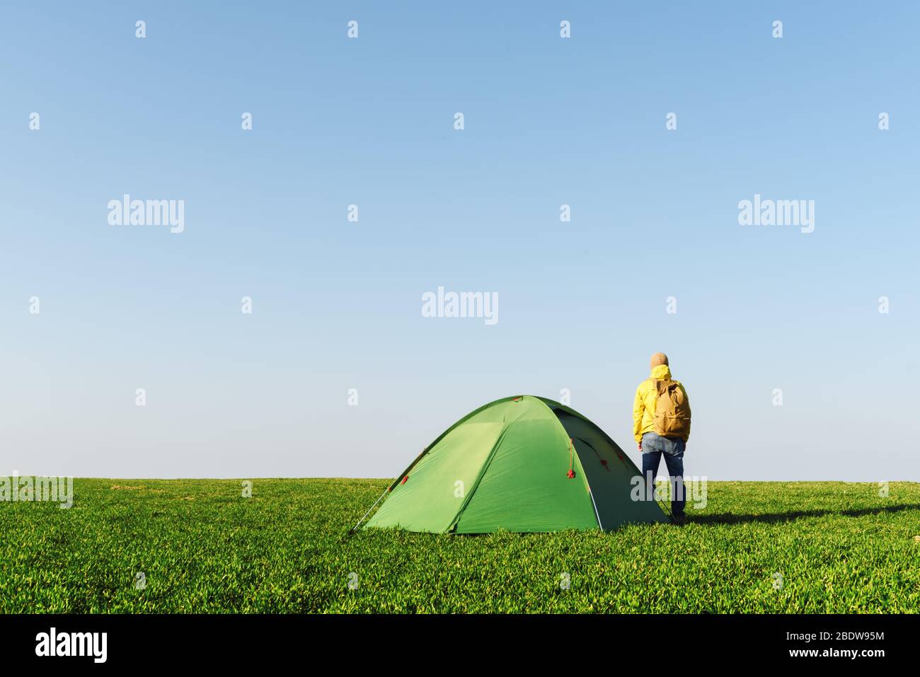 Touriste en veste jaune près de sa tente sur le terrain d'été. Ciel bleu clair. Concept de voyage et d'aventure Banque D'Images