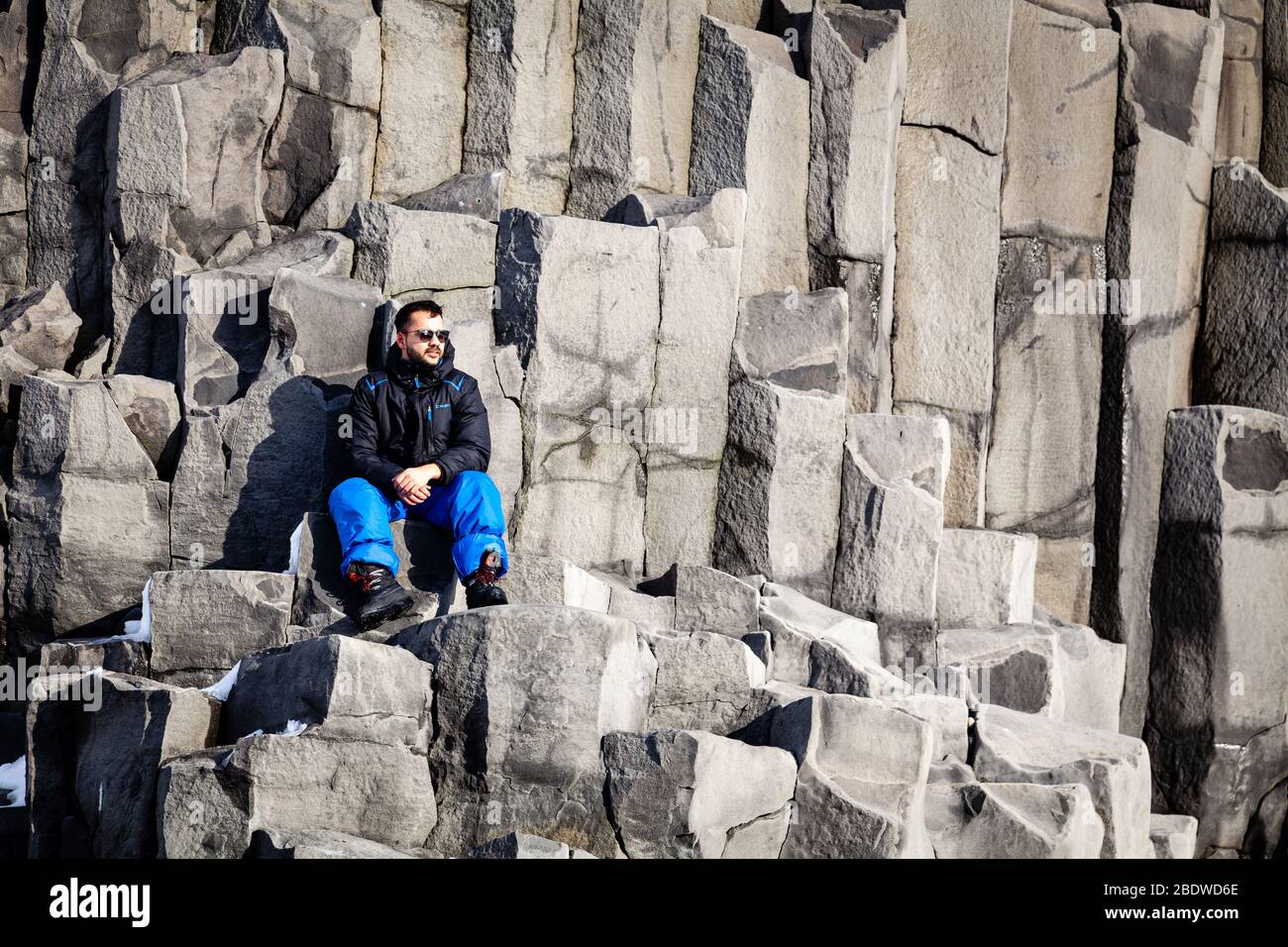 Un homme est assis sur des colonnes de basalte à la plage de sable noir Reynisfjara en hiver près de Vík í Mýrdal, dans le sud de l'Islande Banque D'Images