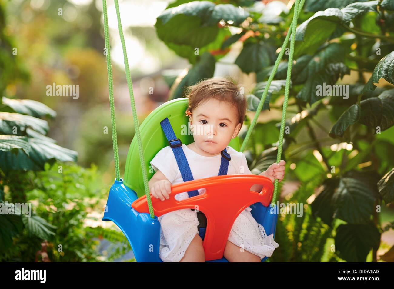Portrait de la fille de bébé sur des balançoires dans le jardin flou arrière-plan Banque D'Images