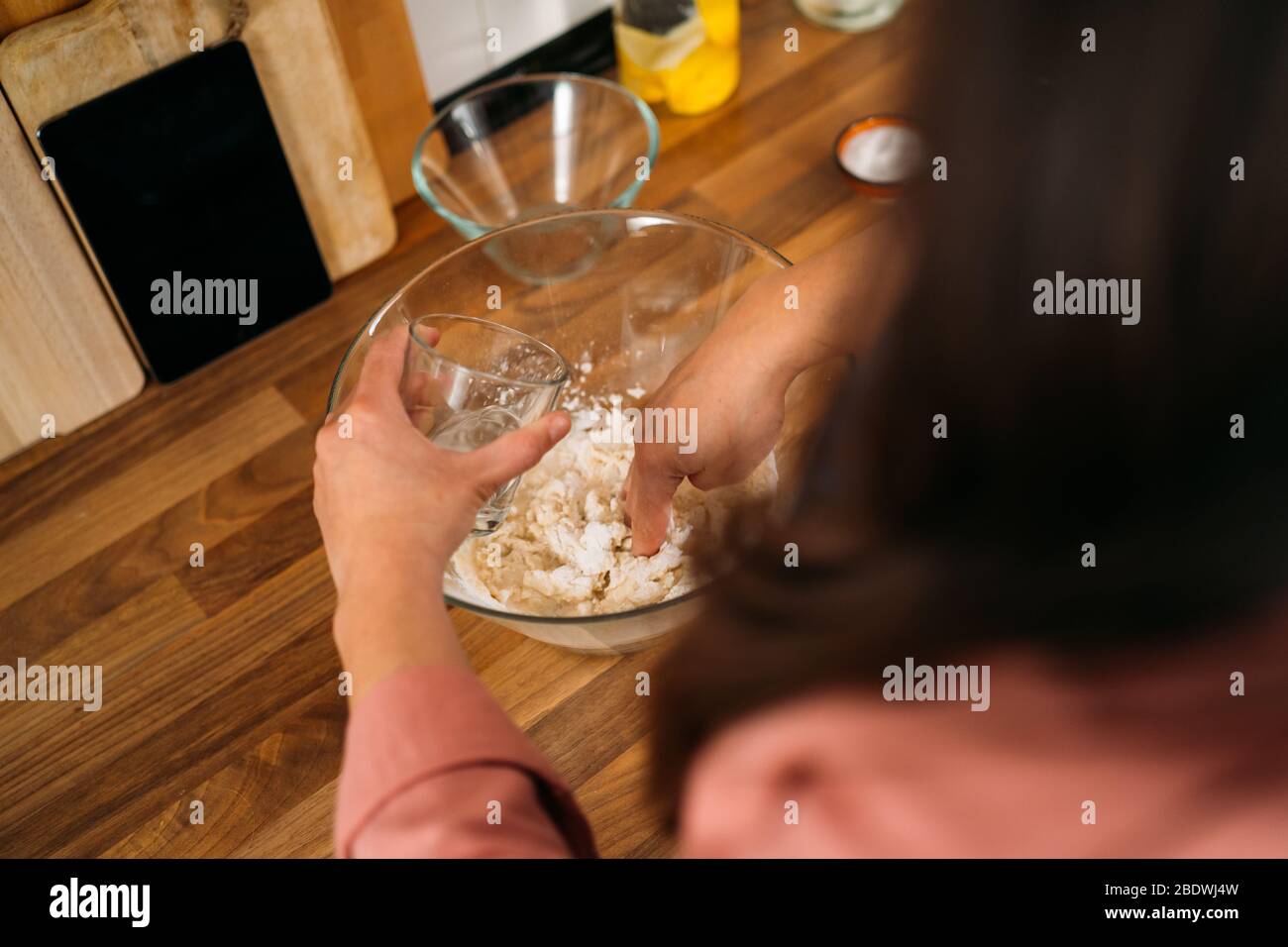 Femme versant un peu d'eau dans un bol avec de la farine et pétrir pour faire une pâte pour pizza dans sa cuisine maison Banque D'Images