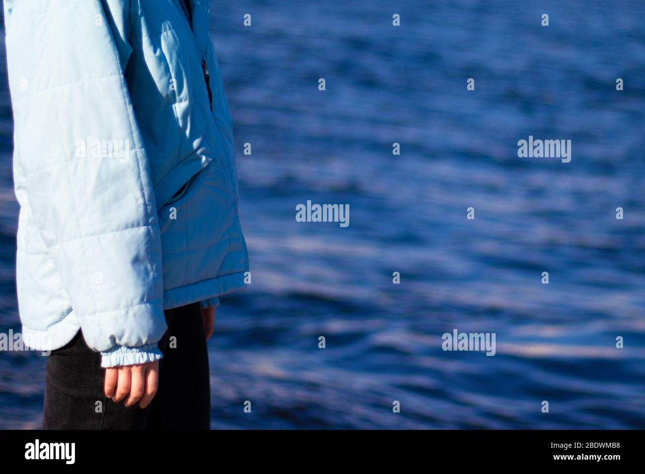 Vue latérale de la femme dans une veste sur fond d'eau bleue. Espace de copie. Ambiance mélancolie Banque D'Images