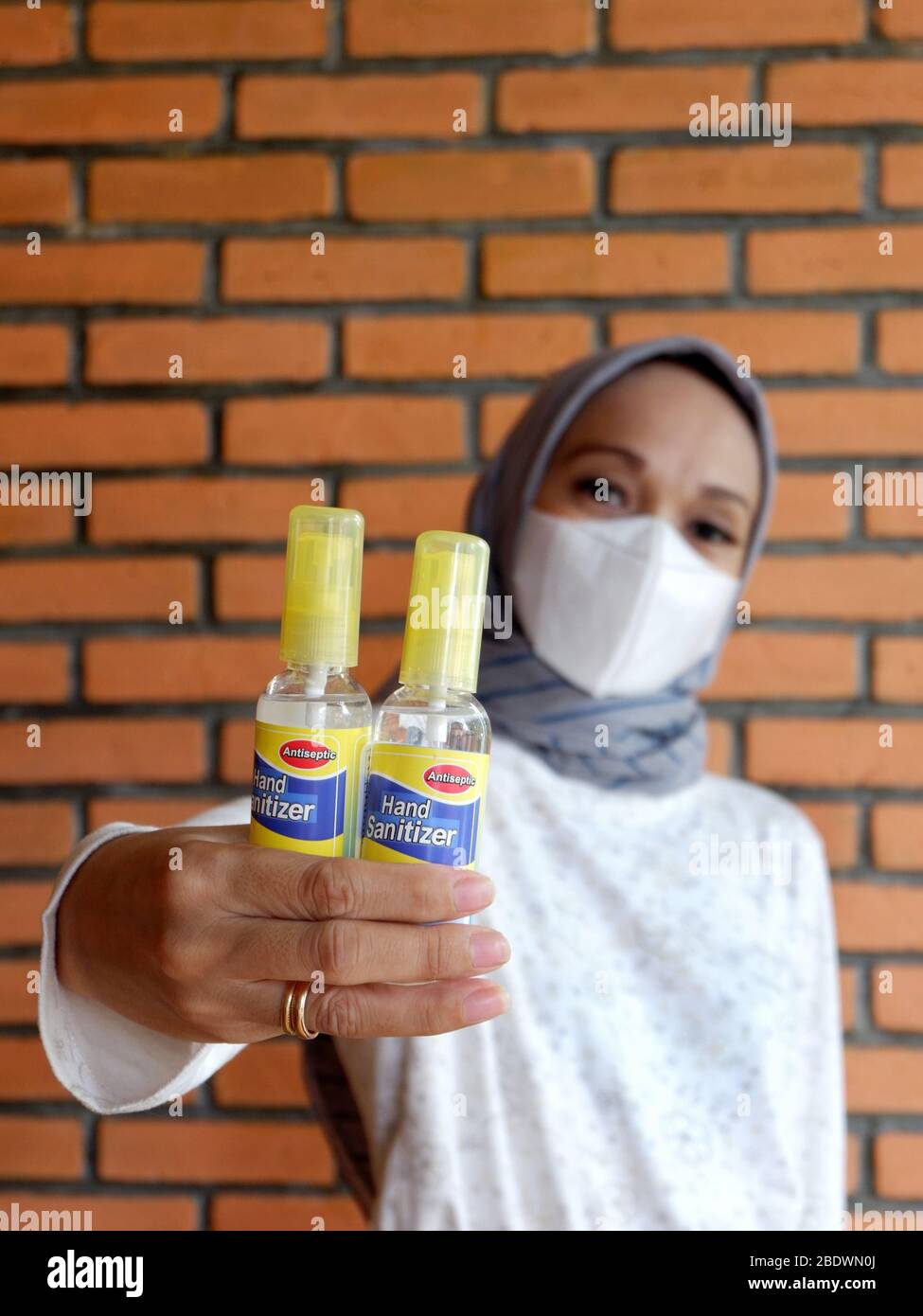 Deux bouteilles de désinfectant pour les mains qui sont détenues par une femme musulmane avec masque de protection (pas au centre). Banque D'Images