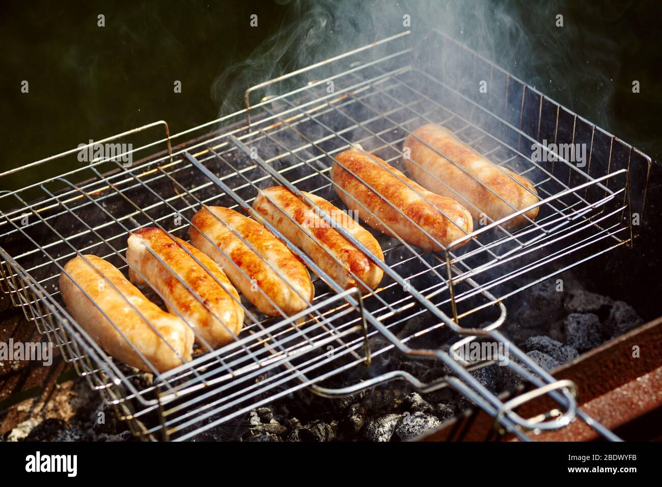 les saucisses de caoutchouc sont rôties sur des charbons. Barbecue sur le gril dans la fumée. Banque D'Images
