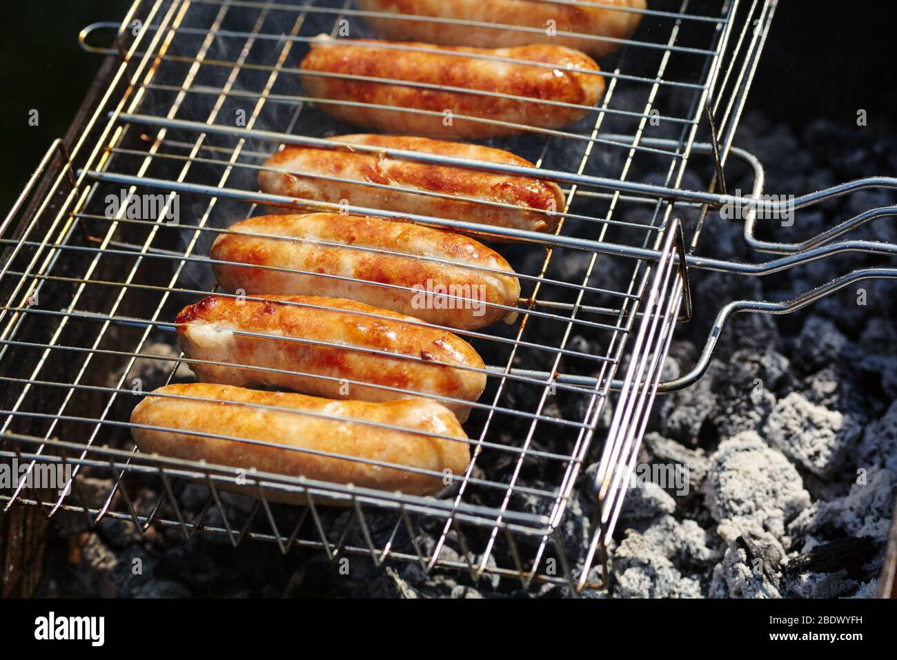 les saucisses de caoutchouc sont rôties sur des charbons. Barbecue sur le gril dans la fumée. Banque D'Images