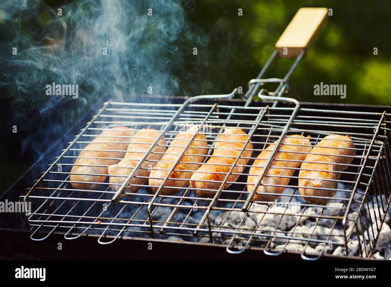 les saucisses de caoutchouc sont rôties sur des charbons. Barbecue sur le gril dans la fumée. Banque D'Images