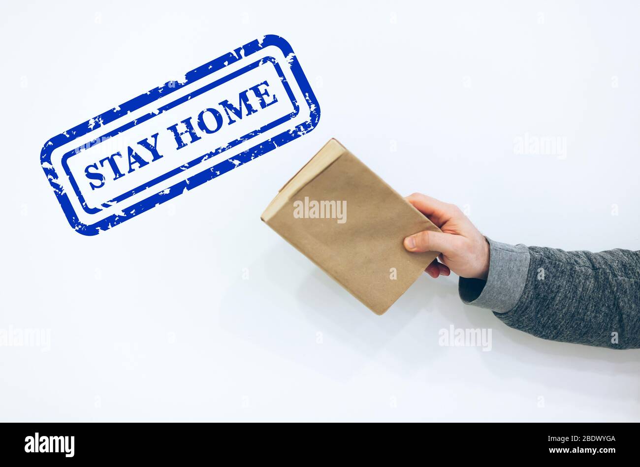 Concept de quarantaine pour rester à la maison: Jeune homme tenant fermer l'ancien livre de papier sur fond blanc avec le cachet bleu de rester à la maison au-dessus de lui Banque D'Images