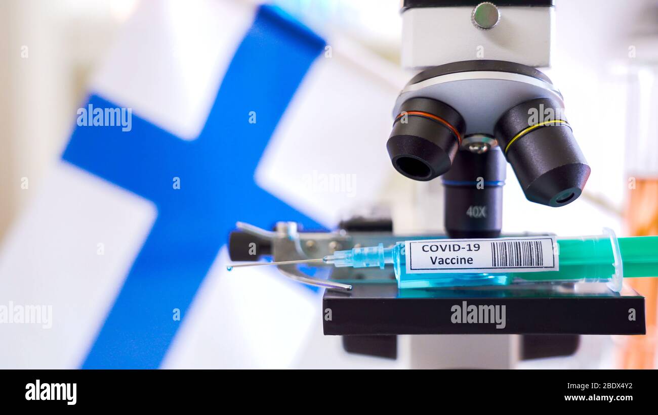 Le regard plus étroit du microscope avec la seringue COVID-19 du vaccin contre le coronavirus sur le stade et le drapeau finlandais sur le dos Banque D'Images