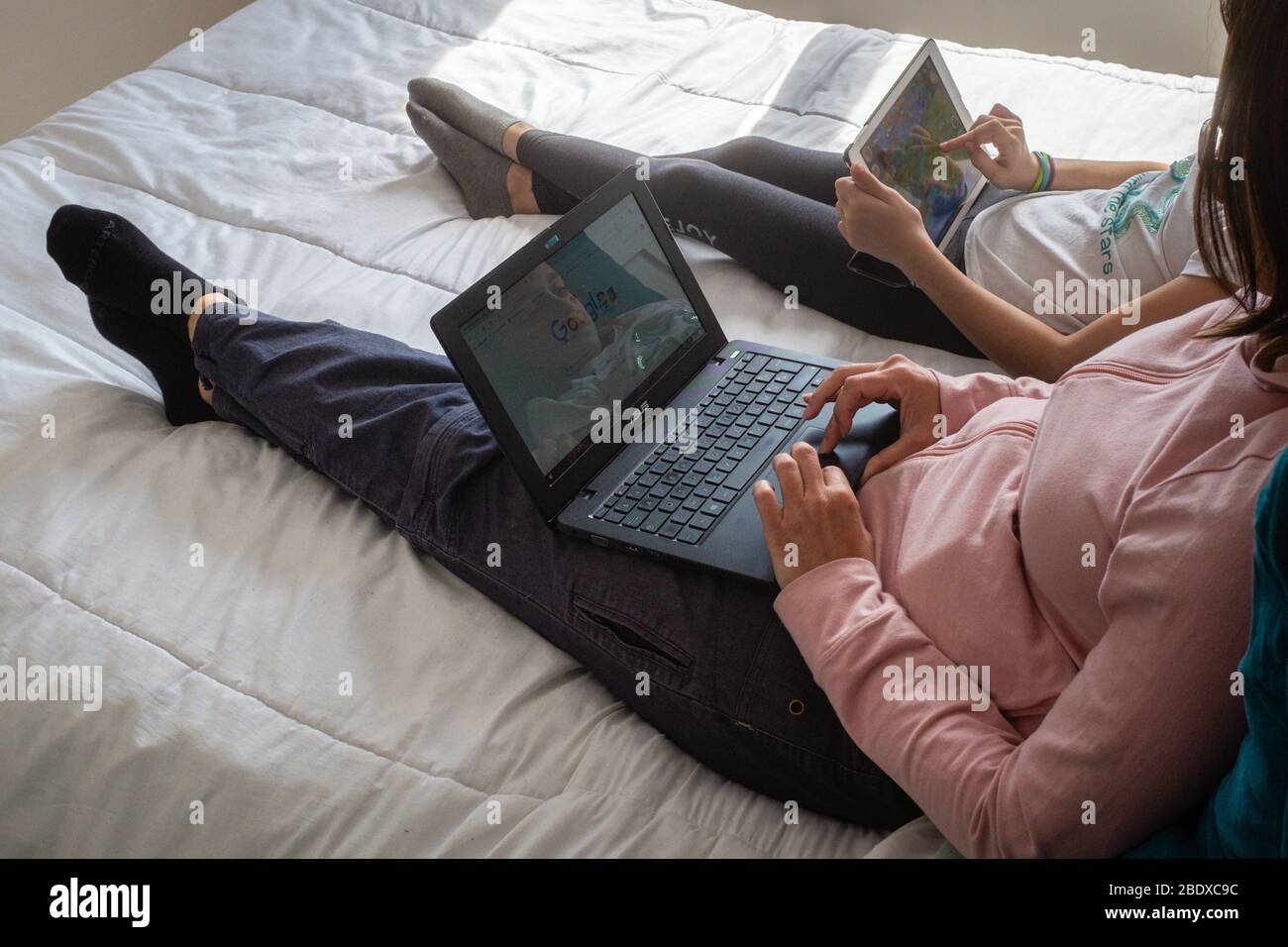 Une mère et un enfant sur un lit avec des ordinateurs pendant la séquestration. Banque D'Images