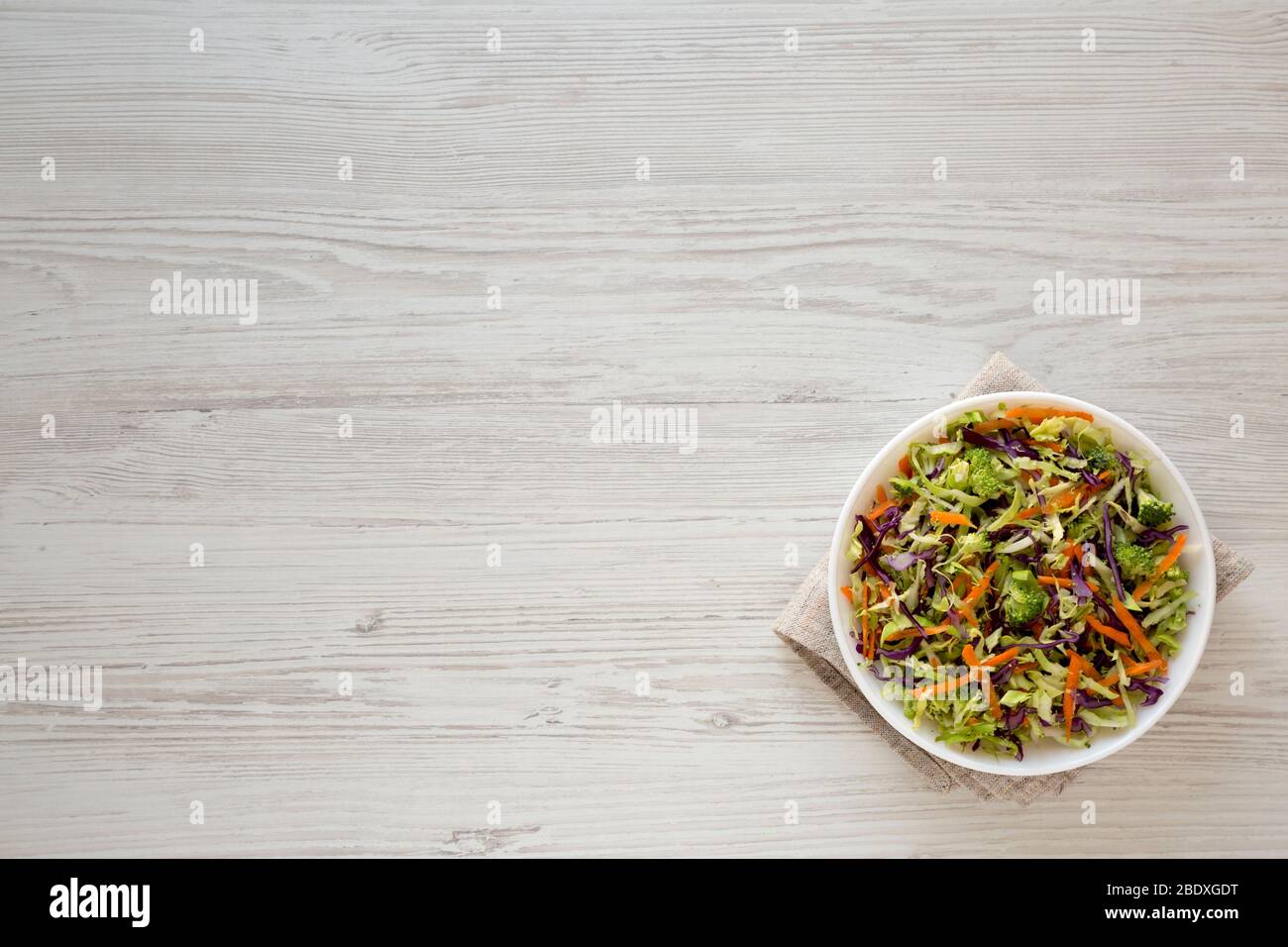 Broccoli Slaw déchiqueté maison dans un bol blanc sur fond blanc en bois, vue de dessus. En hauteur, par dessus, plat. Espace pour le texte. Banque D'Images