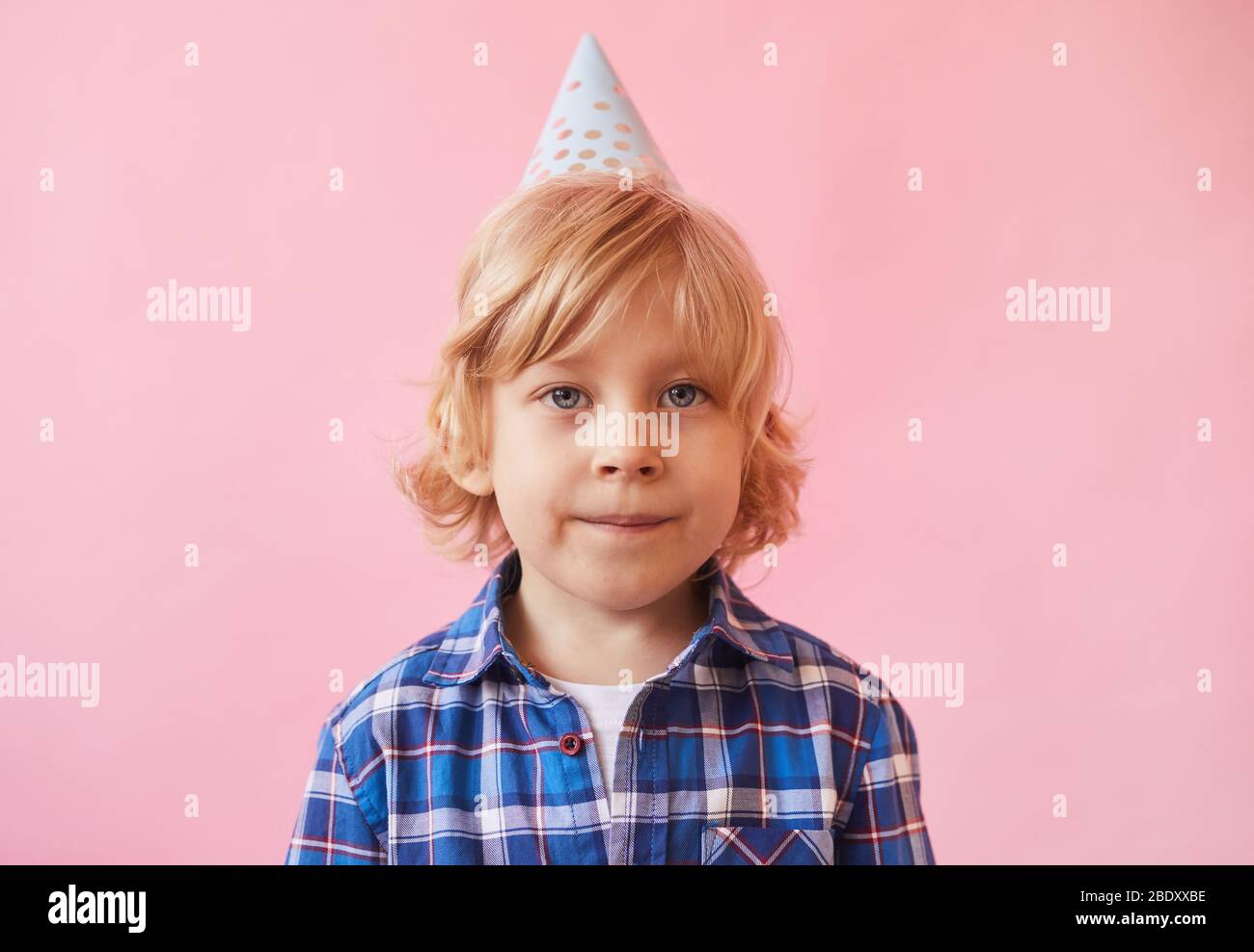 Portrait de petit garçon avec cheveux blond et dans chapeau de fête regardant l'appareil photo sur fond rose Banque D'Images