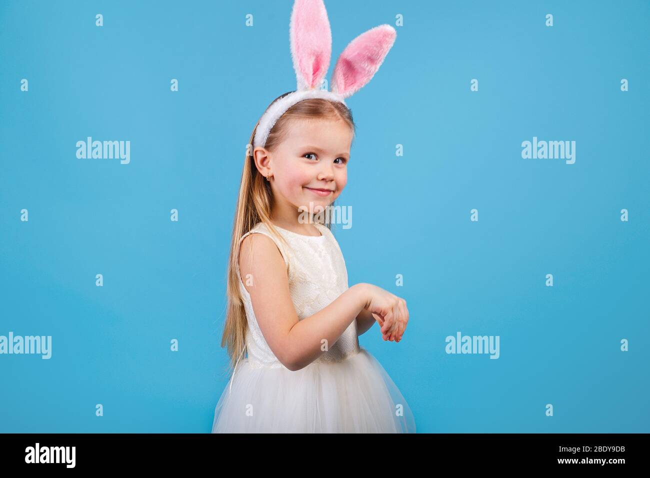 Jolie petite fille porte des oreilles de lapin sur fond bleu. Banque D'Images