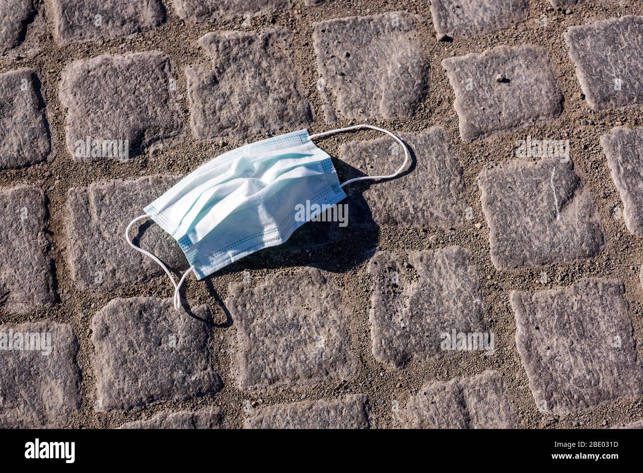 La fin du virus Corona. Masque de protection jeté sur la route pavée. Banque D'Images