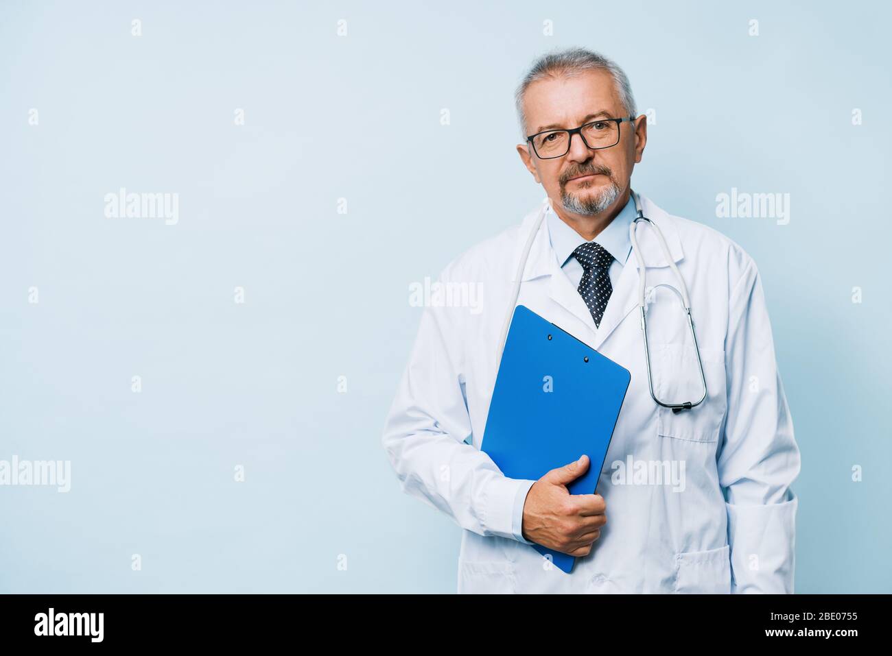 Médecin de sexe masculin âgé barbu en uniforme blanc avec stéthoscope avec dossier bleu. Médecin sur le fond d'un laboratoire de recherche médicale. Banque D'Images