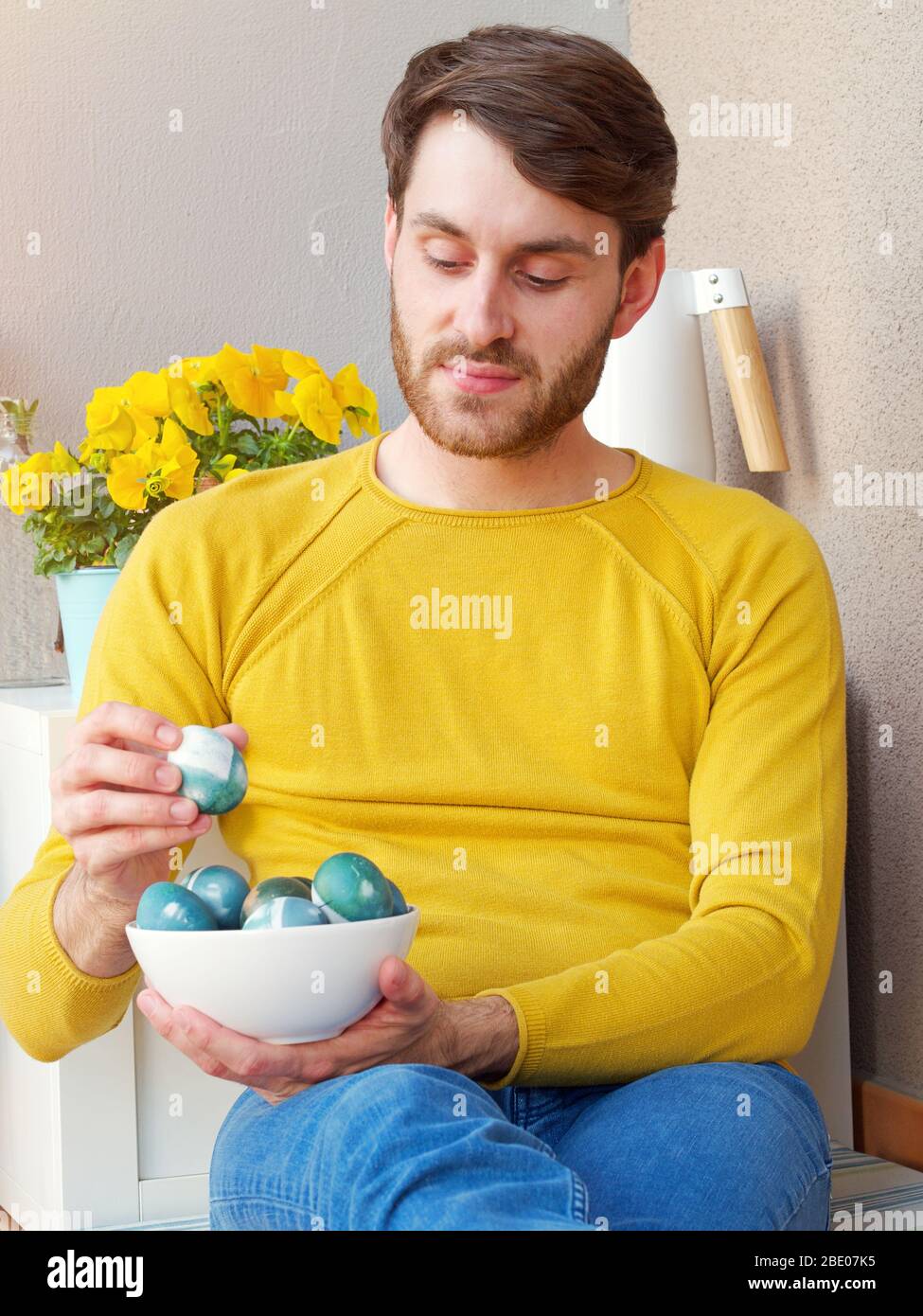 Homme caucasien tenant un bleu des oeufs de pâques dans un bol pendant les temps de pâques, coloré avec la coloration naturelle du chou rouge, portant une bruyère jaune. Banque D'Images