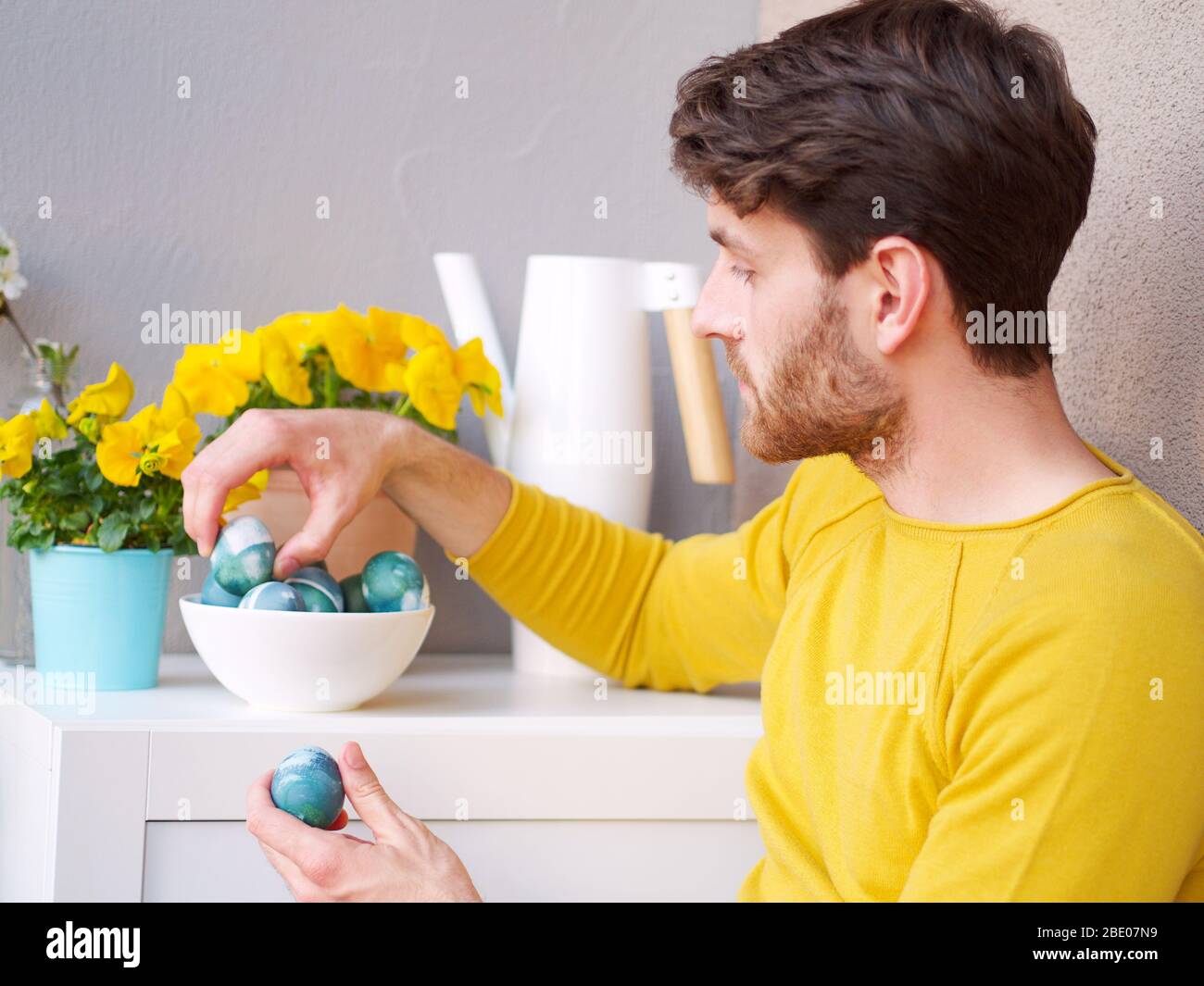 Homme caucasien tenant un bleu des oeufs de pâques dans un bol pendant les temps de pâques, coloré avec la coloration naturelle du chou rouge, portant une bruyère jaune. Banque D'Images