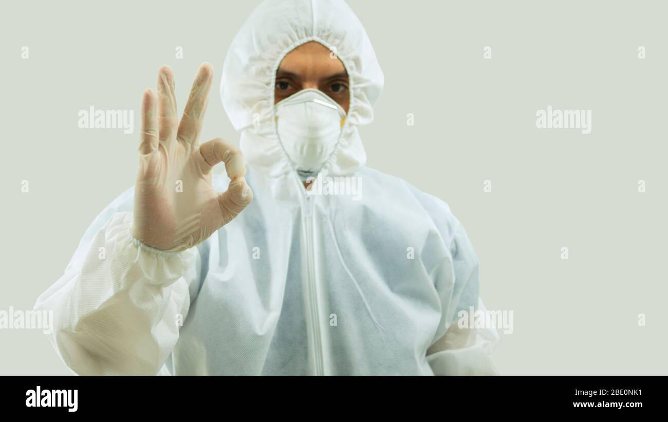 Vue avant du médecin avec masque et costume de bioprotection avec bras étendu vers l'avant et sa main droite faisant un signe OK sur fond blanc Banque D'Images