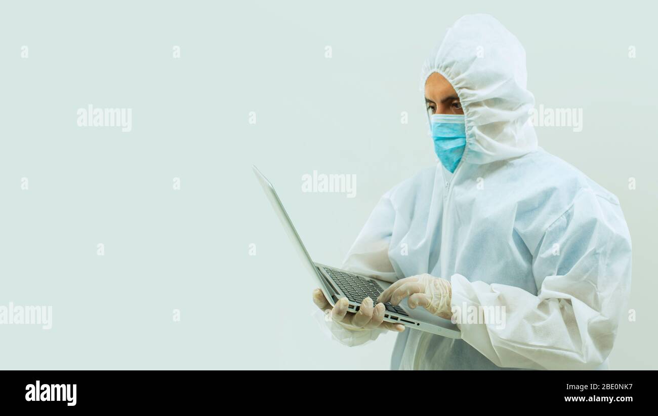 Médecin en costume blanc de bioprotection et masque bleu tenant avec ses mains un ordinateur portable ouvert sur fond blanc Banque D'Images