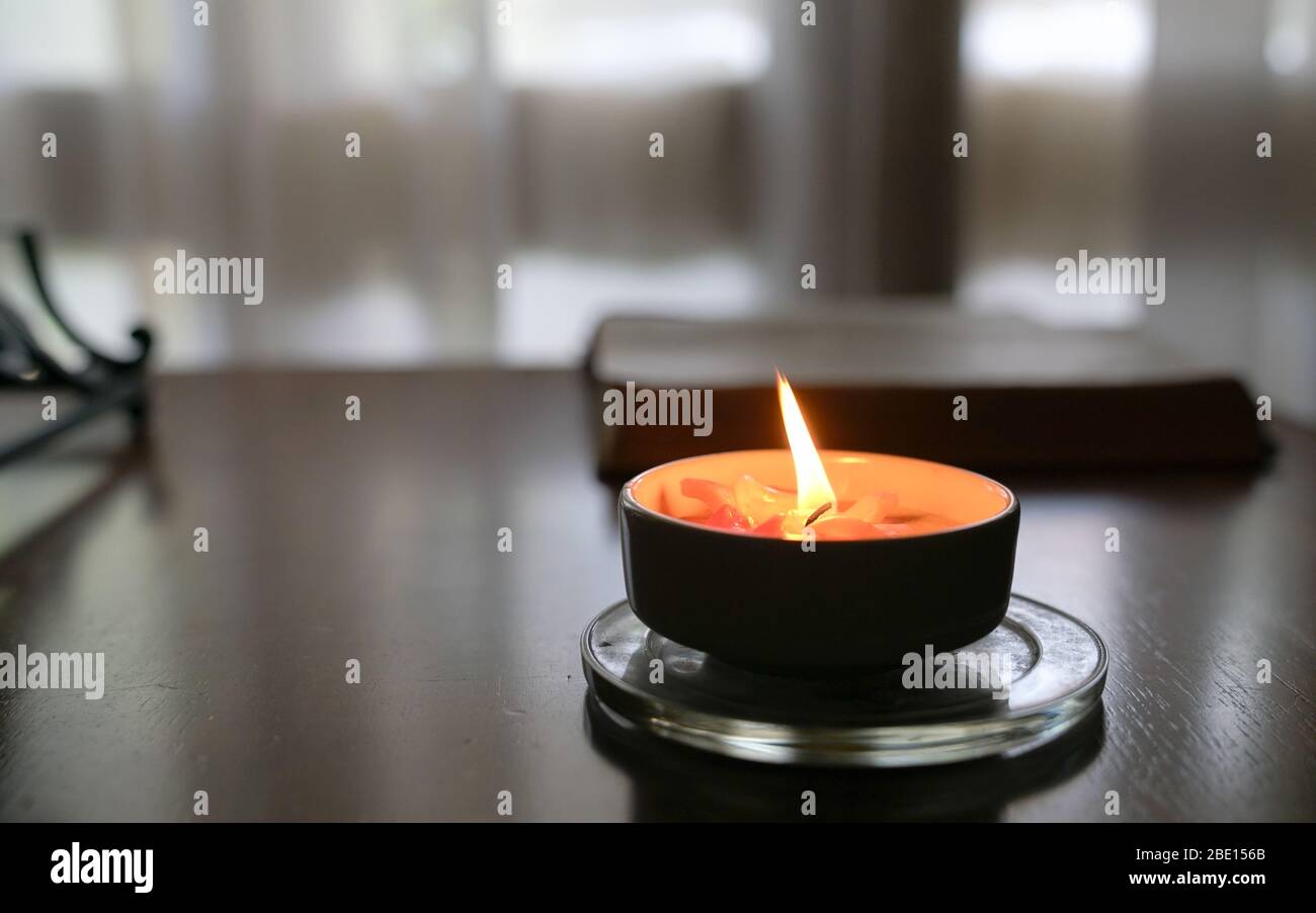 Bougie brûlante sur la table avec livre et rideau à l'arrière-plan. Banque D'Images