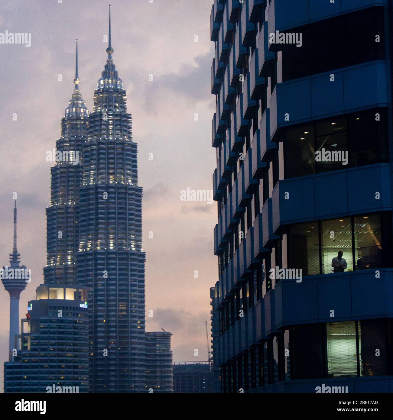 Photo en début de soirée des tours Petronas avec un immeuble de bureaux et un ouvrier en silhoueté au premier plan à Kuala Lumpur, en Malaisie. Banque D'Images