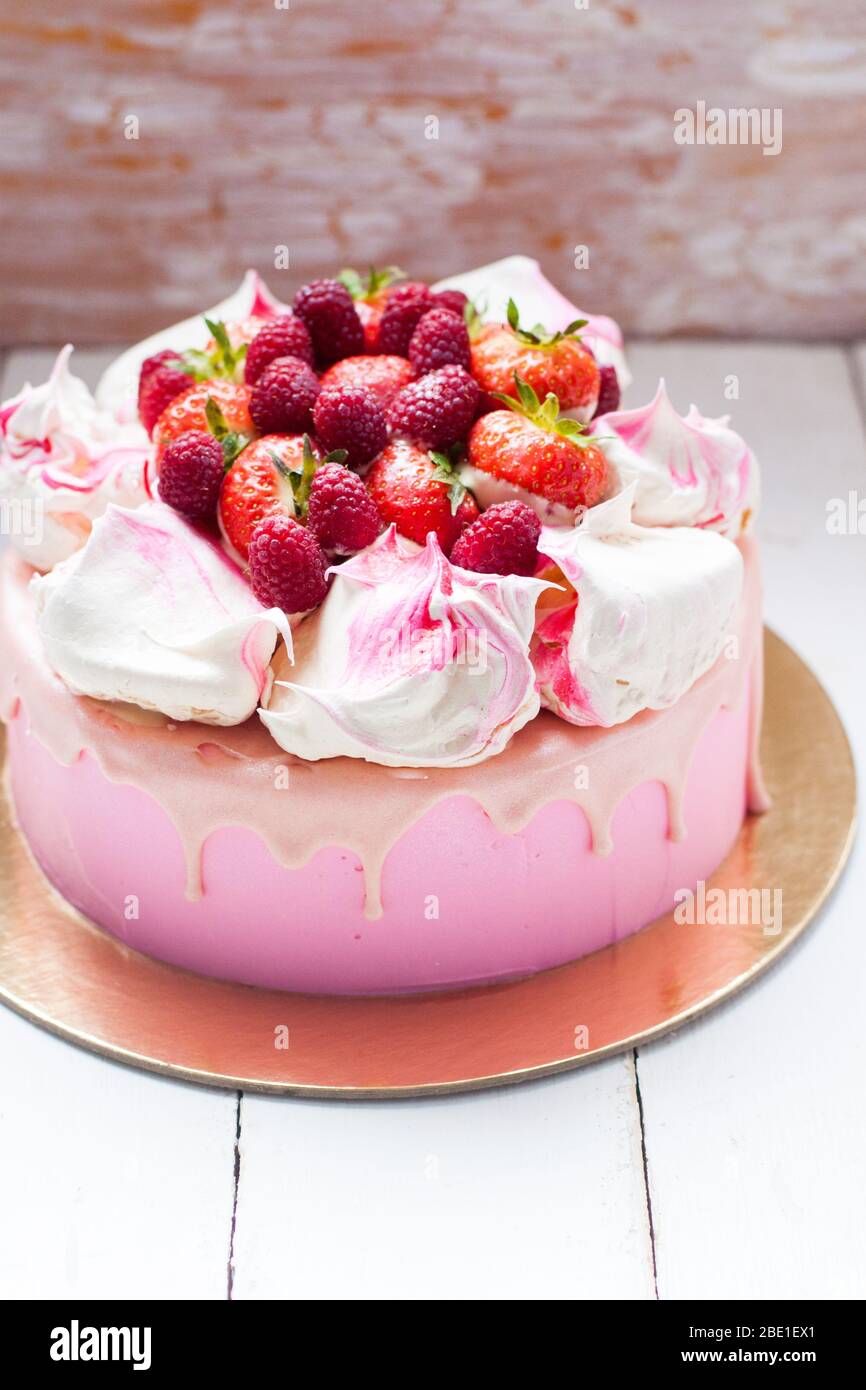 Gâteau rose avec meringue, chocolat fondu et framboises et fraises fraîches. Arrière-plan rustique. Banque D'Images