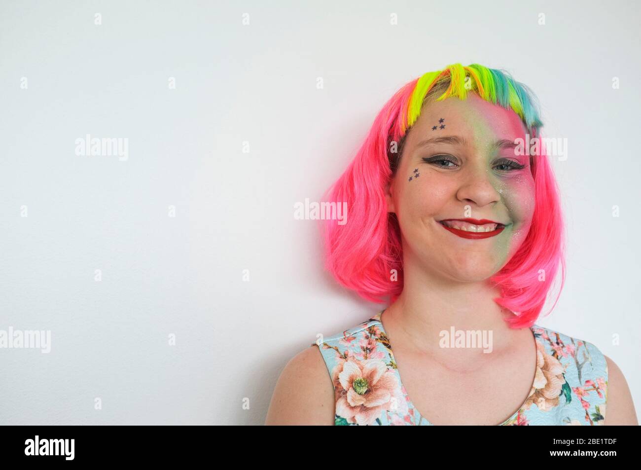 Une adolescente avec une perruque multicolore et un lourd appoint contre un mur blanc. Banque D'Images