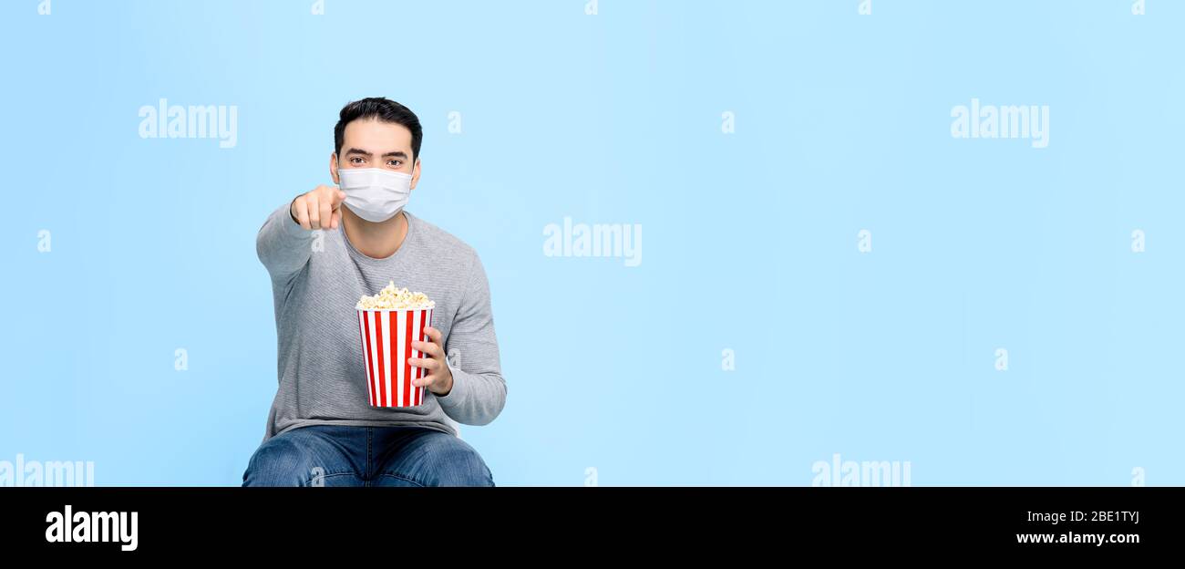 Jeune homme avec popcorn se protègent en portant un masque médical tout en regardant un film isolé sur fond bleu bannière avec espace de copie Banque D'Images