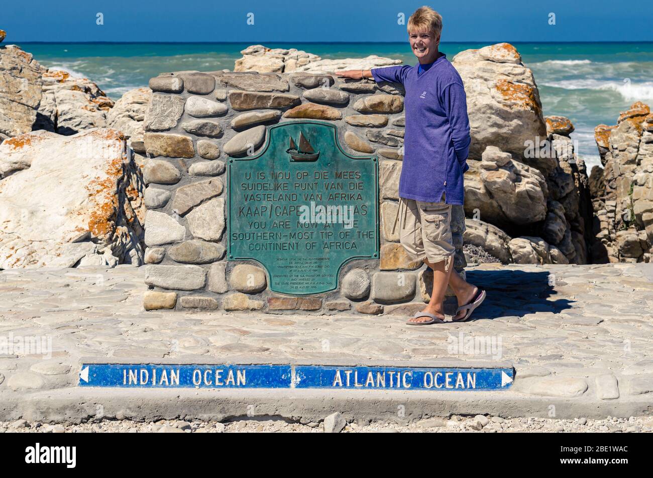 Femme posant pour photo sur le monument en pierre à la pointe sud de l'Afrique où l'Atlantique rencontre l'océan Pacifique Cape Agulis point Afrique du Sud Banque D'Images