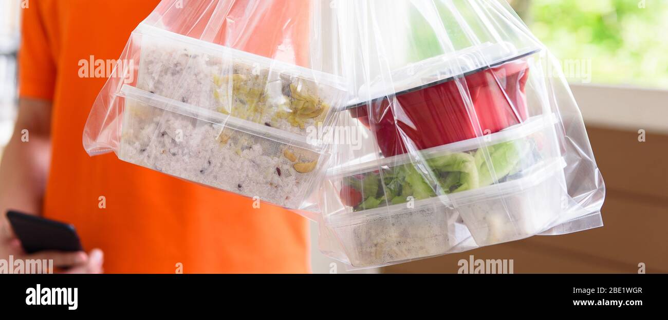 Image panoramique des boîtes alimentaires asiatiques dans des sacs en plastique livrés au client à la maison par l'homme de livraison Banque D'Images