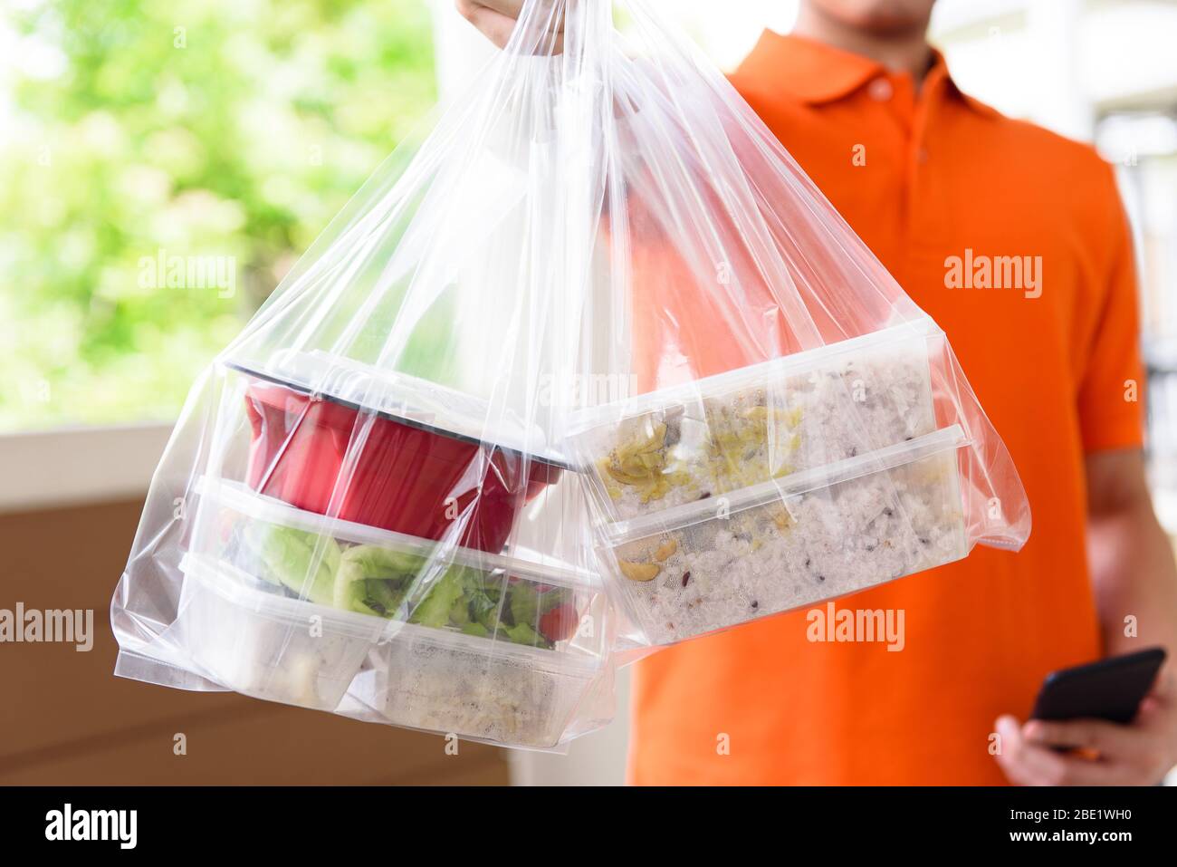 Nourriture asiatique dans des boîtes à emporter livrées au client à la maison par le liveur homme en uniforme orange Banque D'Images