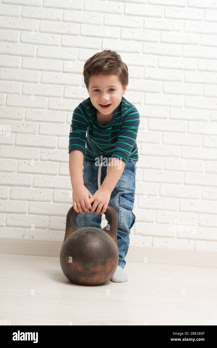 Un petit garçon essaie de soulever une bouilloire en fer Banque D'Images