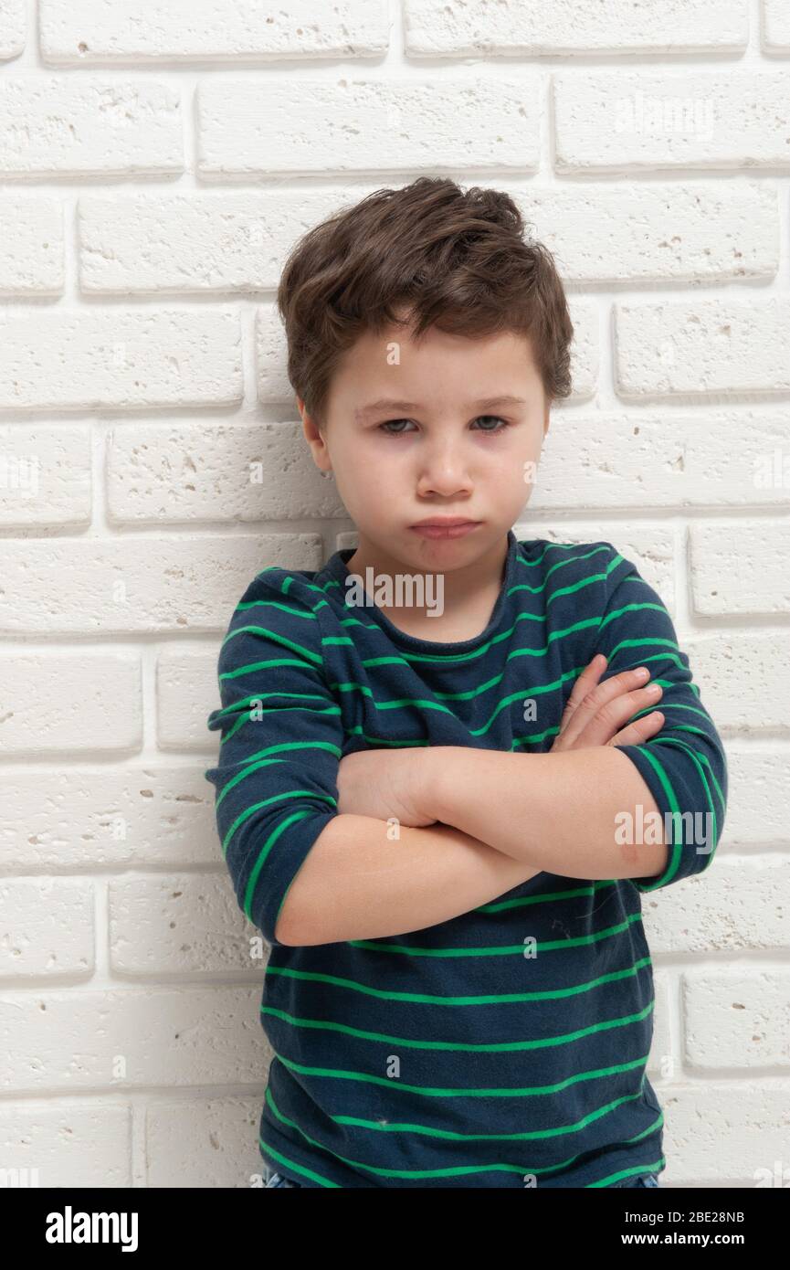 Un garçon en colère frognant sur fond de mur de briques. Banque D'Images