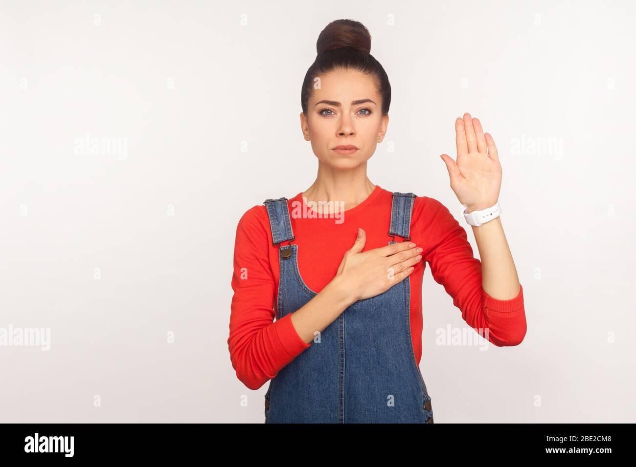 Je vous promets ! Portrait de la fille honnête digne de confiance avec un pain de cheveux dans des salopettes en denim soulevant la paume pour jurer l'allégeance, responsable et patriotique personne. ind Banque D'Images