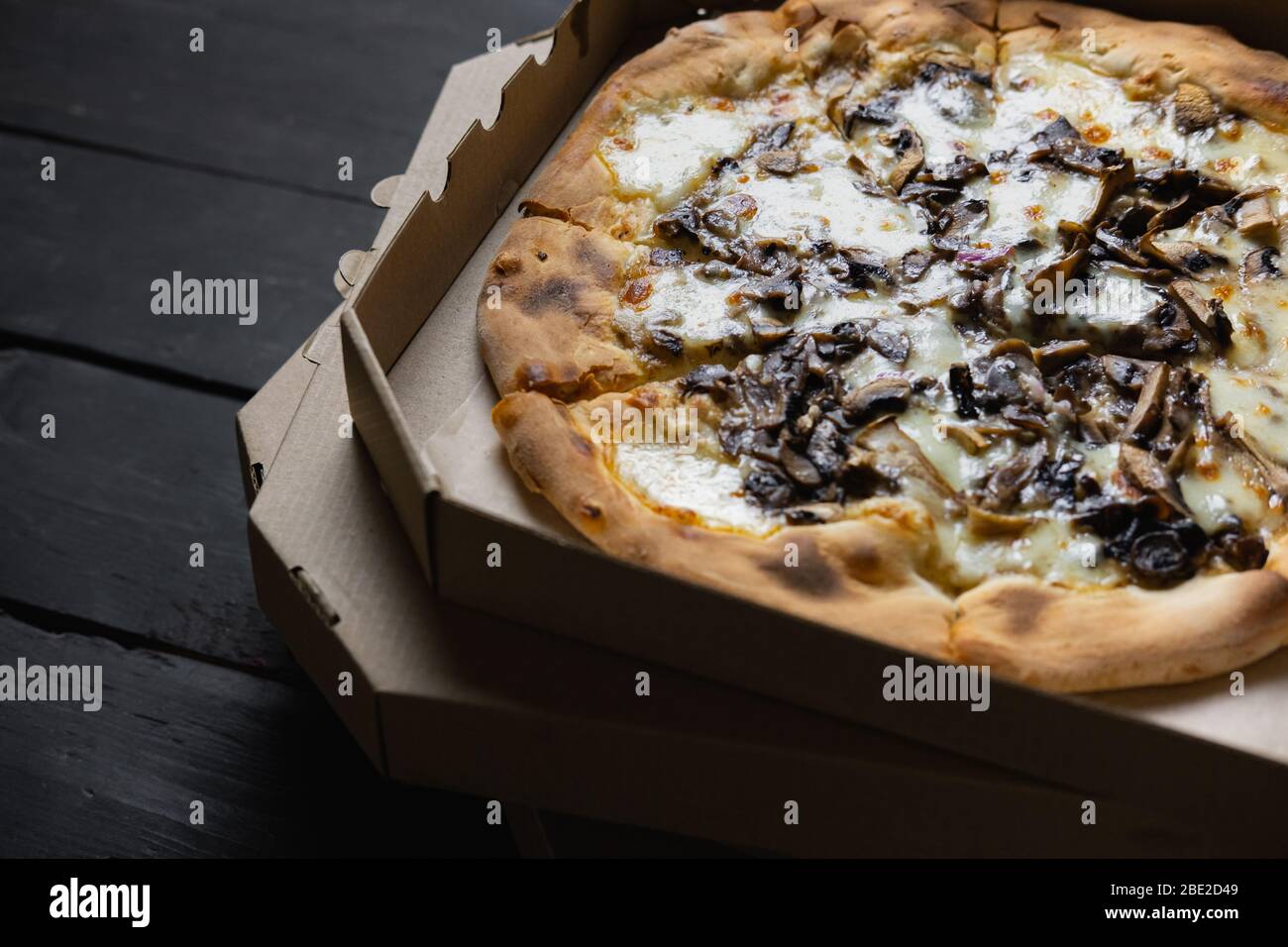 Pizza funghi dans une boîte de livraison ouverte. Alimentation à emporter, concept de nourriture à emporter : pieu de pizzas aux champignons dans des boîtes sur fond de bois noir Banque D'Images