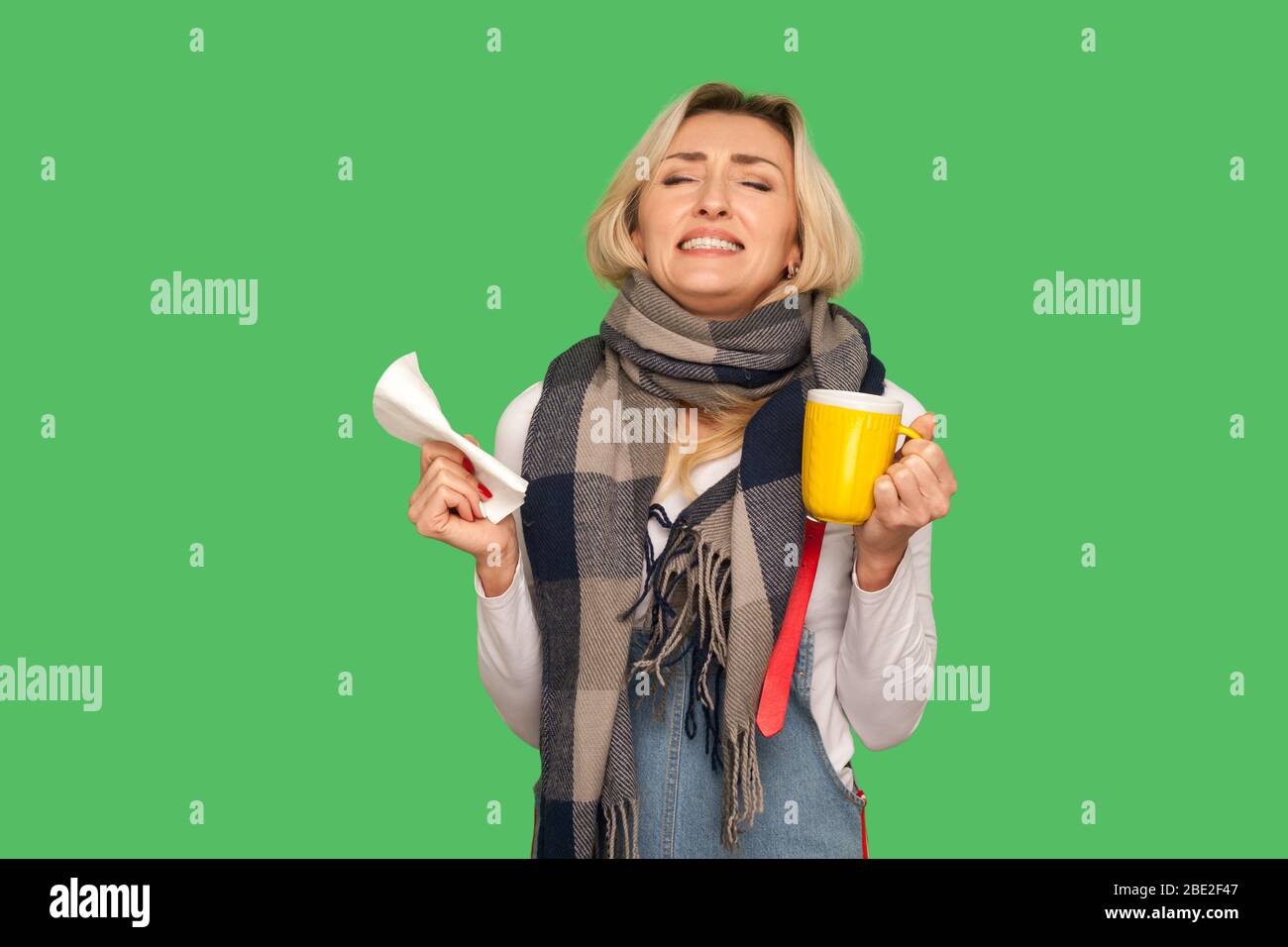 Je déteste avoir la grippe! Portrait d'une femme adulte irritée enveloppée dans un foulard tenant le thé, la serviette et les dents de claçage avec la colère, se sentant désespérée au sujet de l'influ Banque D'Images