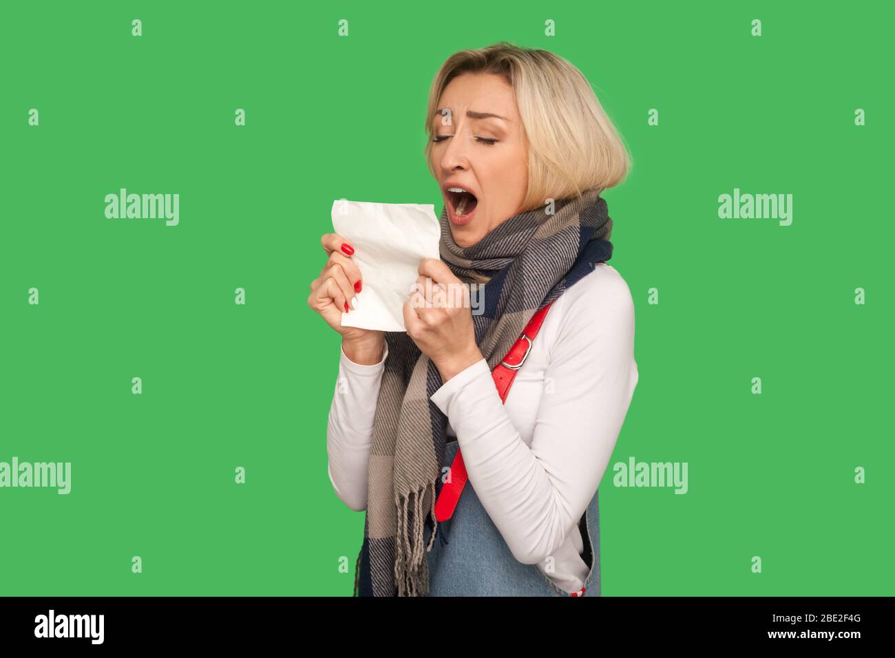 Allergie, nez liquide. Portrait d'une femme adulte malade portant un foulard chaud debout avec une bouche ouverte pour éternuer en serviette, se sentir mal, souffrant de grippe sym Banque D'Images