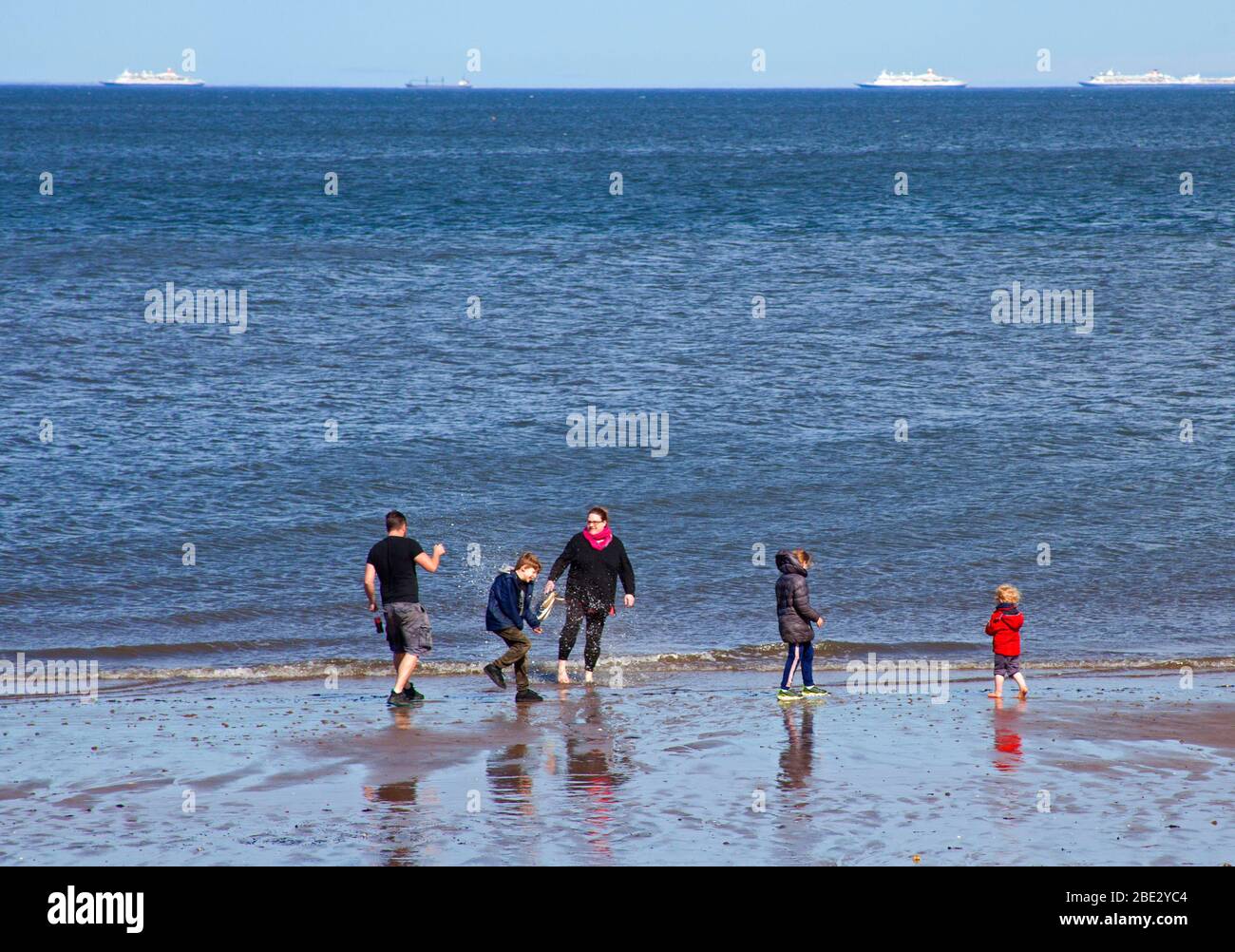 Portobello Promenade, Édimbourg, Écosse, Royaume-Uni. 11 avril 2020. Température de 16 degrés avec plein soleil dans l'après-midi après un début nuageux. Le samedi de Pâques, une plage très calme le troisième week-end de coronavirus Lockdown. Une famille s'amuse au bord de la mer. Banque D'Images