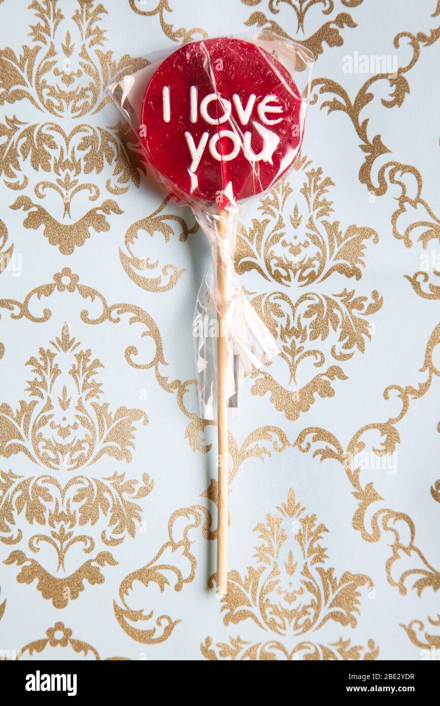 Un doux "Je t'aime" rouge de lypop contre un fond de motif doré et bleu clair, plat, vue sur le dessus, minimaliste Banque D'Images
