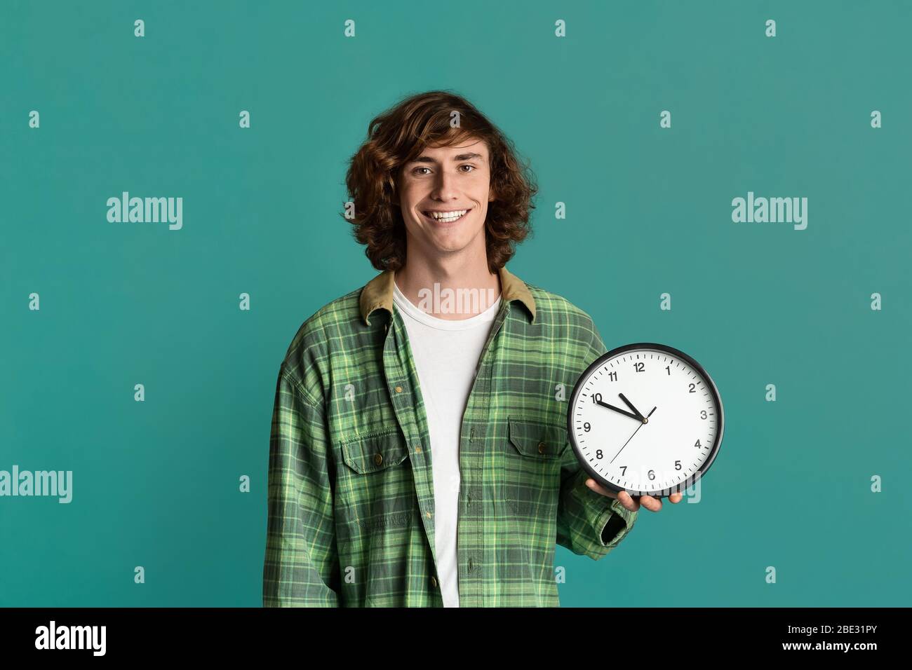 Gestion efficace du temps. Heureux étudiant tenant l'horloge sur fond turquoise Banque D'Images