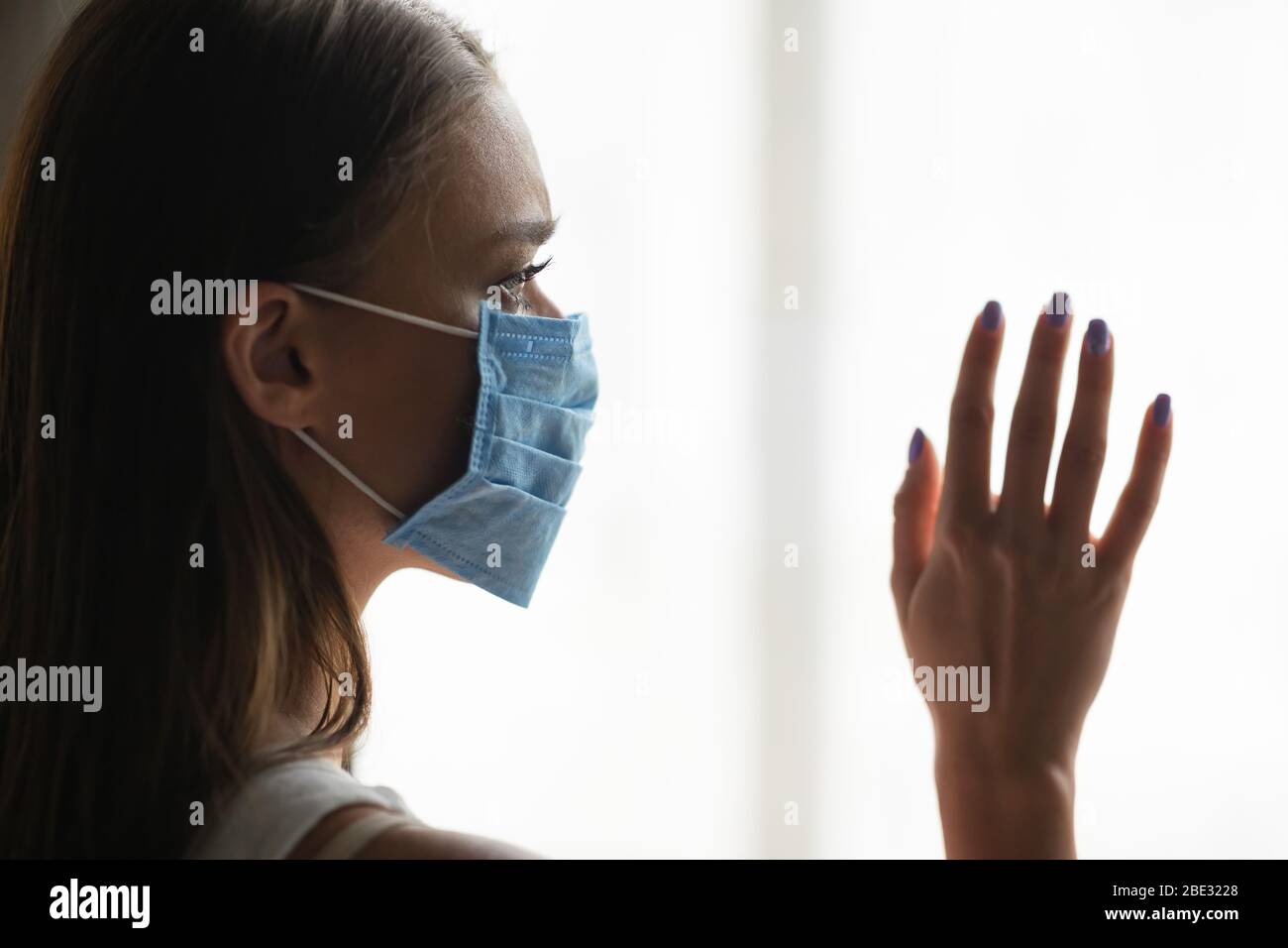 Femme dans un masque de protection debout près de la fenêtre à la maison Banque D'Images