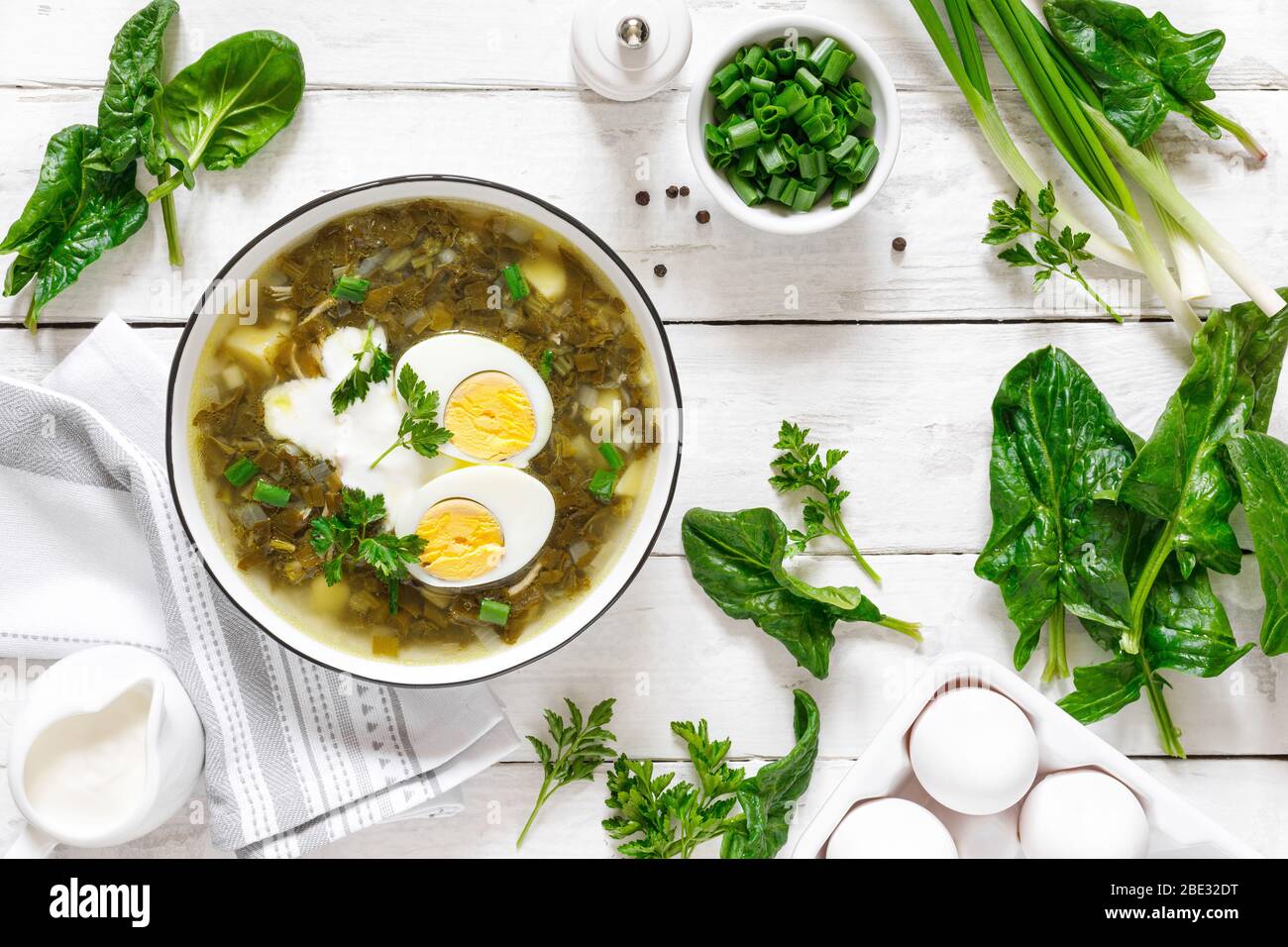 Soupe aux épinards et aux sorrel verts avec œufs durs et crème sure sur table rustique en bois blanc, vue sur le dessus Banque D'Images