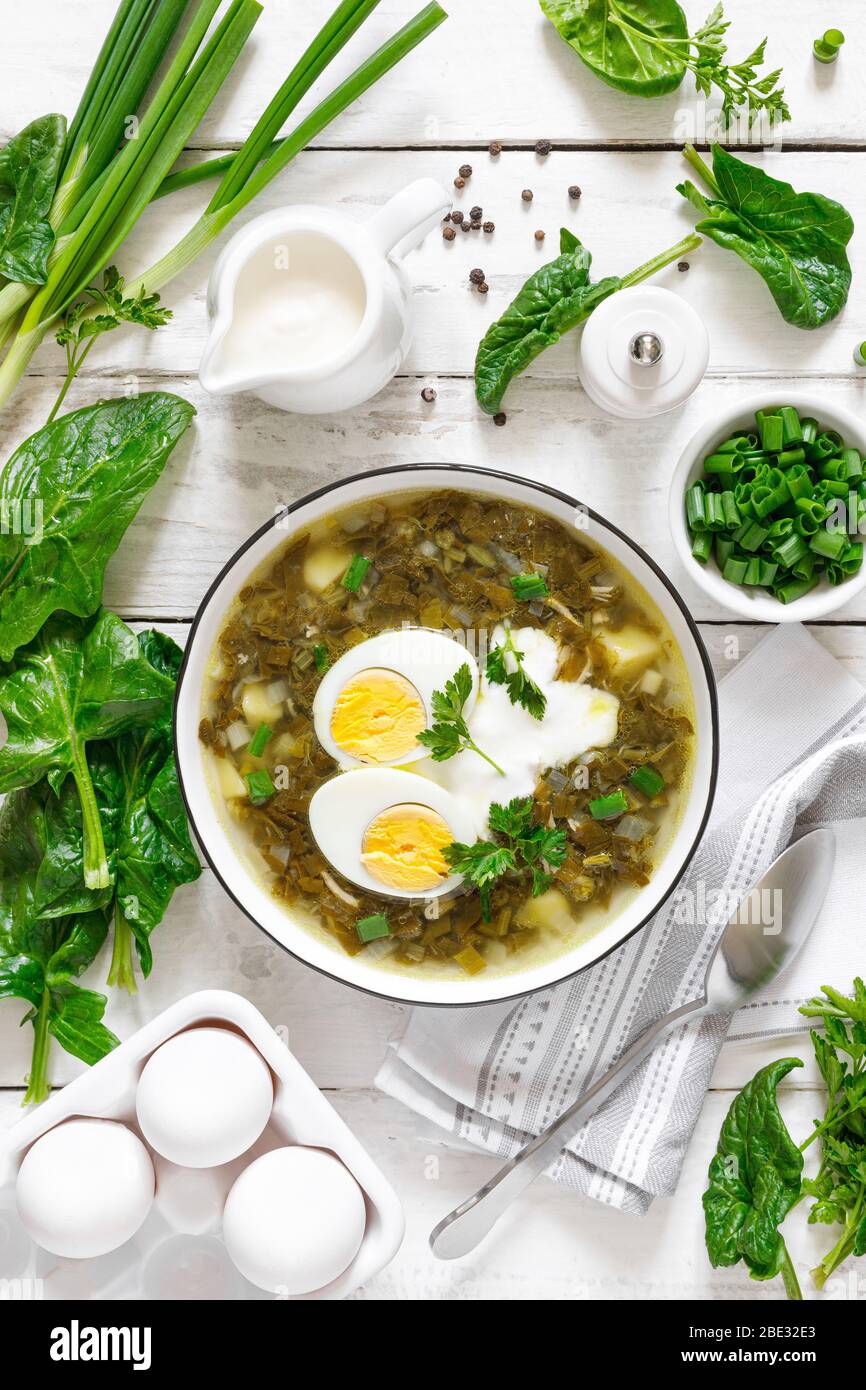 Soupe aux épinards et aux sorrel verts avec œufs durs et crème sure sur table rustique en bois blanc, vue sur le dessus Banque D'Images