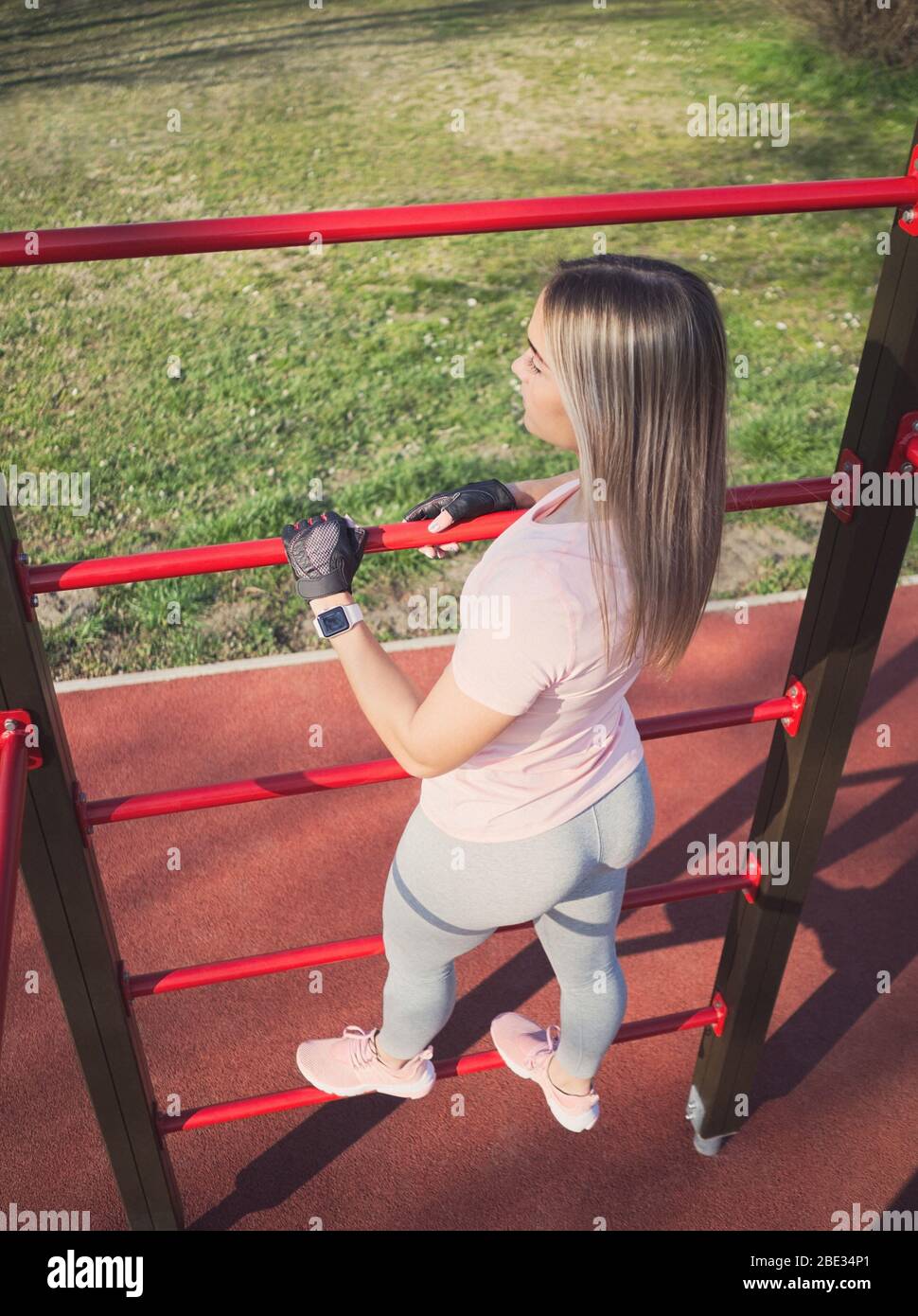 Jeune femme athlétique dans les vêtements de sport posant à Wall bars dans le parc Banque D'Images