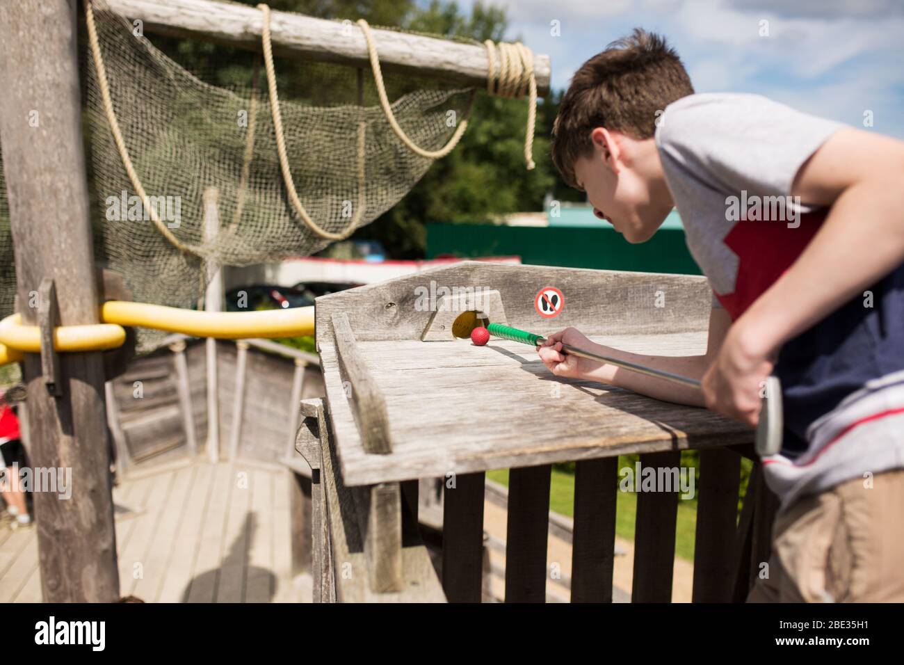 Un garçon de treize ans se prépare à faire une balle de golf dans un tube sur un trou de thème nautique au minigolf de Karlshagen, en Allemagne. Banque D'Images