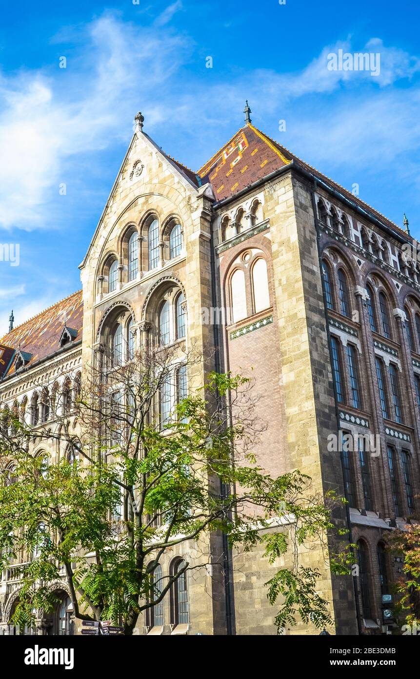 Le beau bâtiment historique des Archives nationales de Hongrie dans la capitale hongroise Budapest. L'extérieur de la maison entouré d'arbres sur une photo verticale avec le ciel bleu au-dessus. Banque D'Images