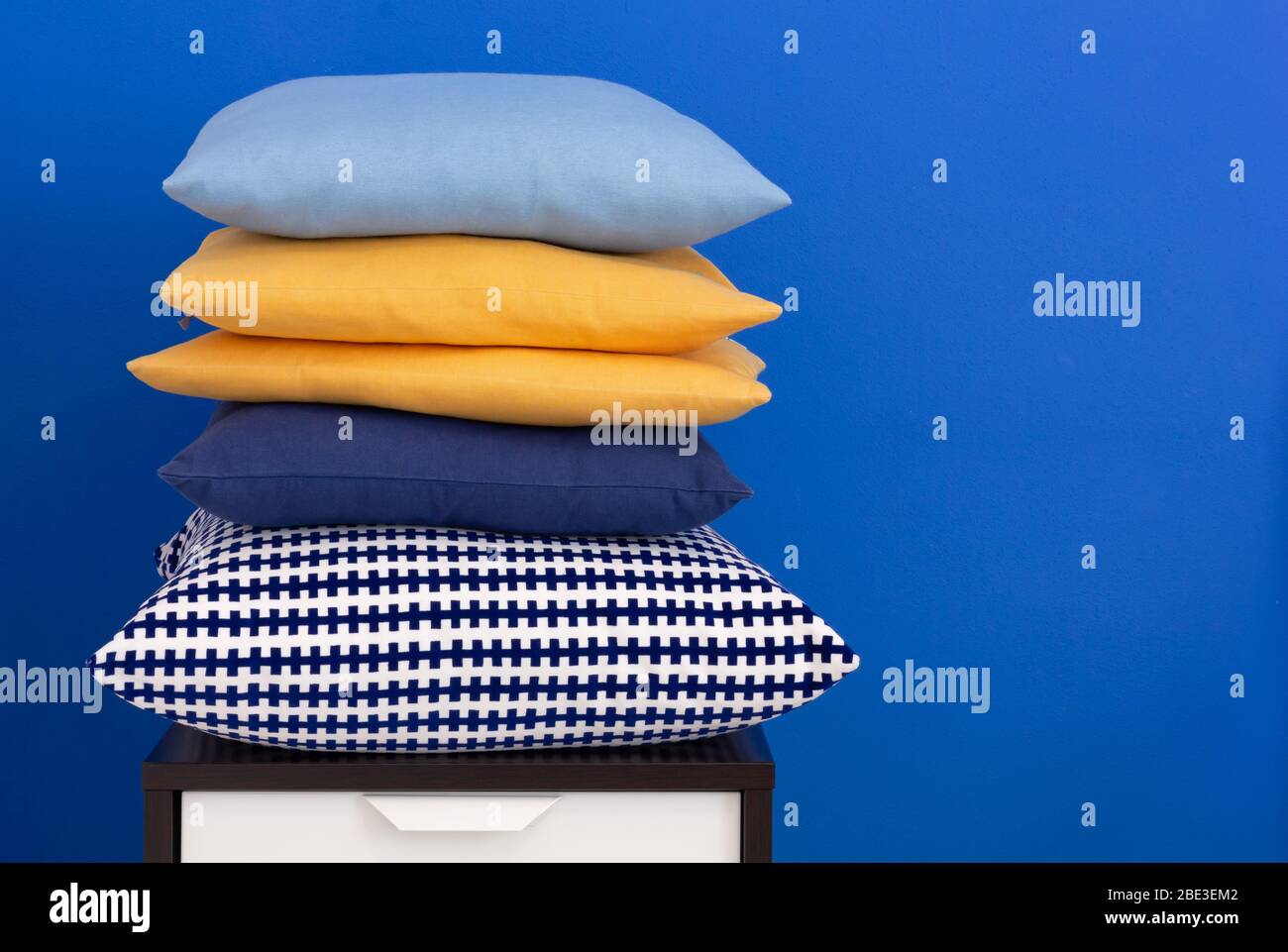 Pile de coussins sur une table de nuit en bois contre un mur intérieur bleu Banque D'Images