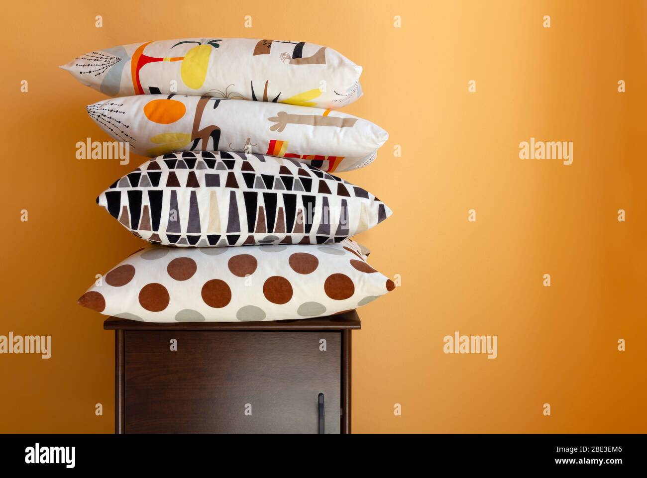 Pile de coussins sur une table de nuit en bois contre un mur intérieur orange Banque D'Images