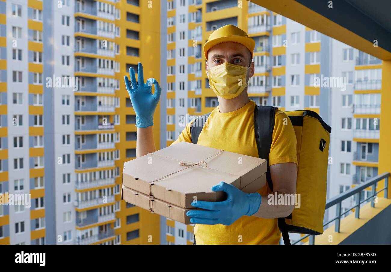 Livraison de nourriture sûre. Le coursier en uniforme jaune, le masque de protection et les gants fournissent des aliments à emporter pendant la quarantaine du coronovirus Banque D'Images