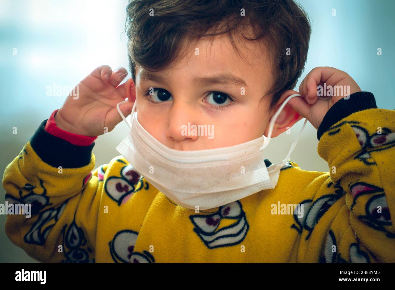 Drôle regardant 3 ans curieux bébé turc en pyjama essayant de porter le masque chirurgical Banque D'Images